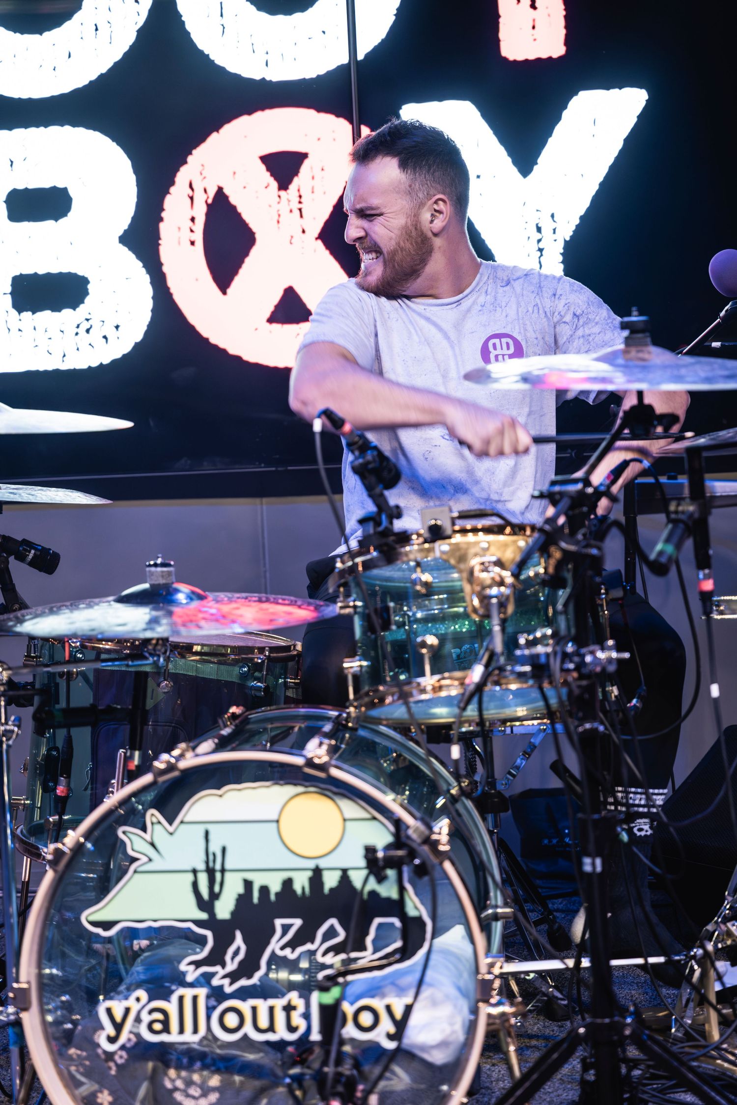 Drummer performs behind custom drum kit with band logo during live show.
