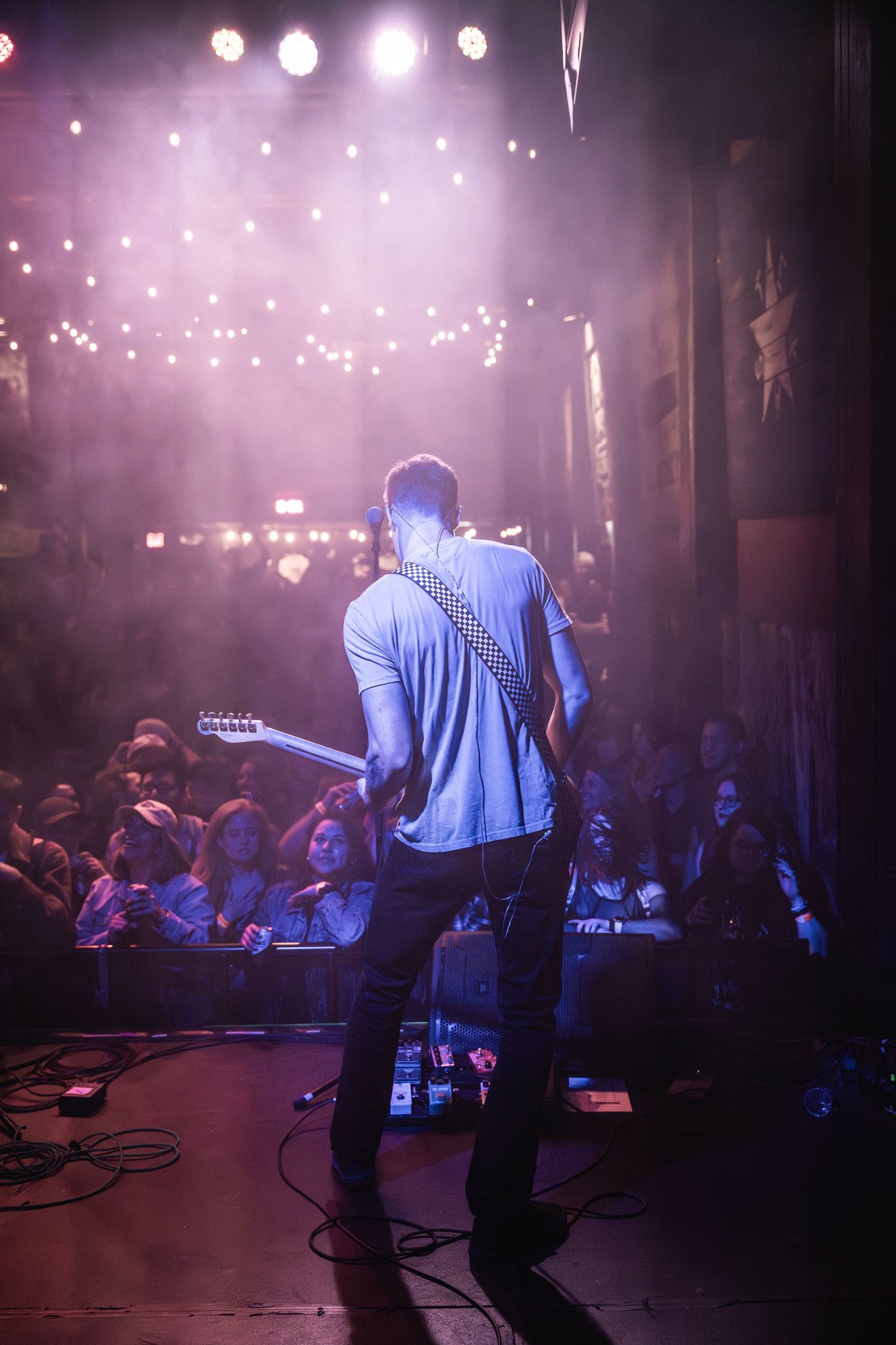 Silhouette of guitarist performing on stage with string lights and purple atmospheric lighting.