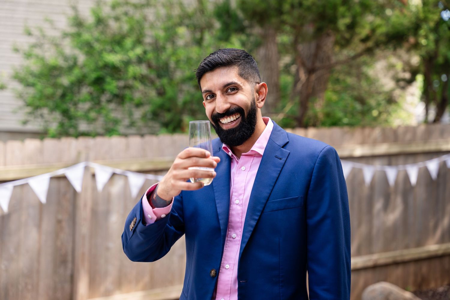 A guest in a blue suit and pink shirt enjoying a celebratory moment at an outdoor party.