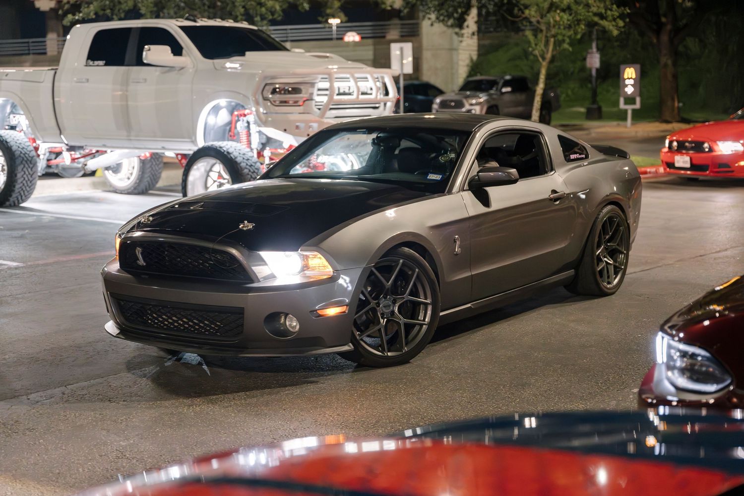 Gray Mustang sports car with custom wheels parked at night with LED headlights illuminated.