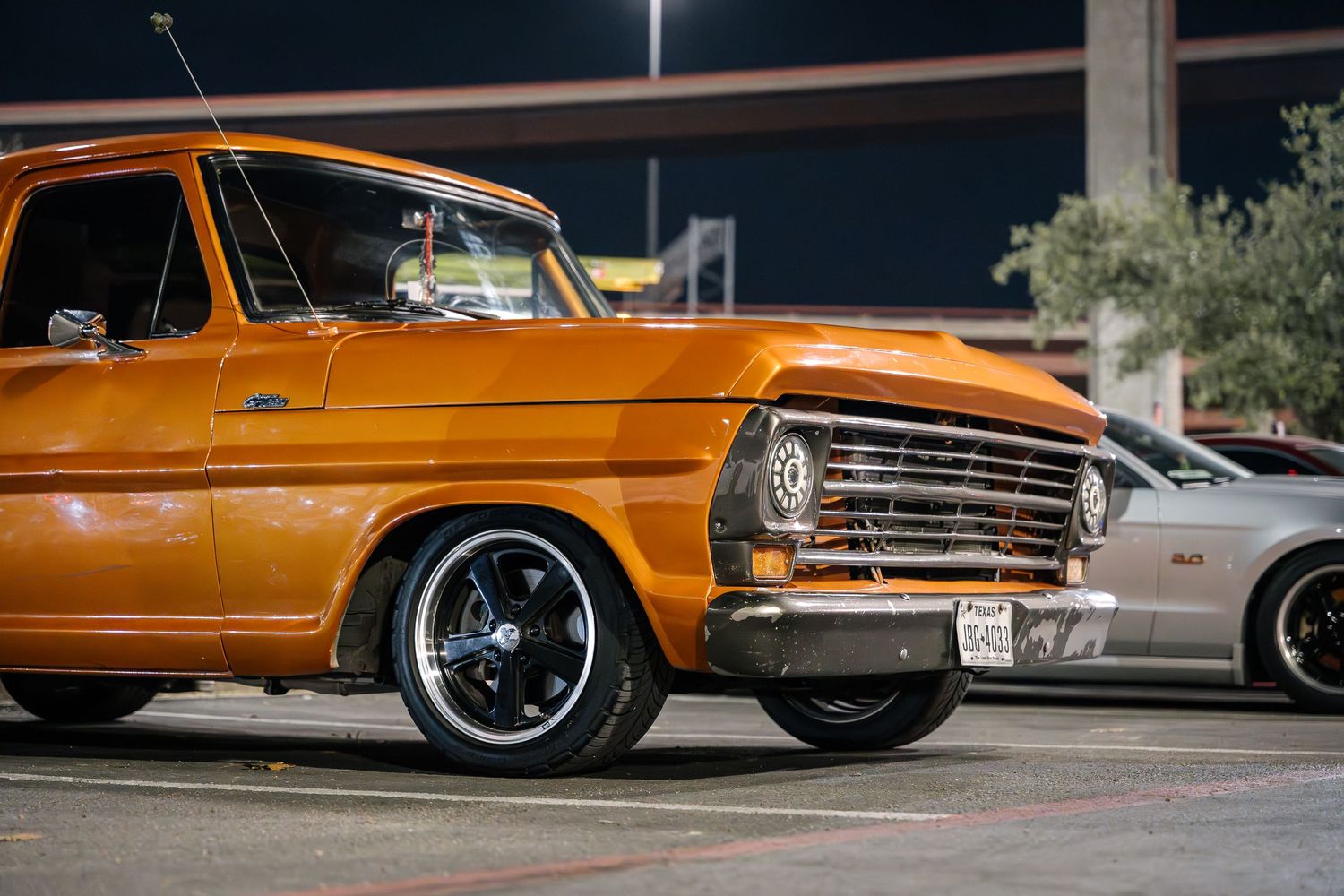Classic Ford pickup in orange showcases custom wheels and lowered suspension.