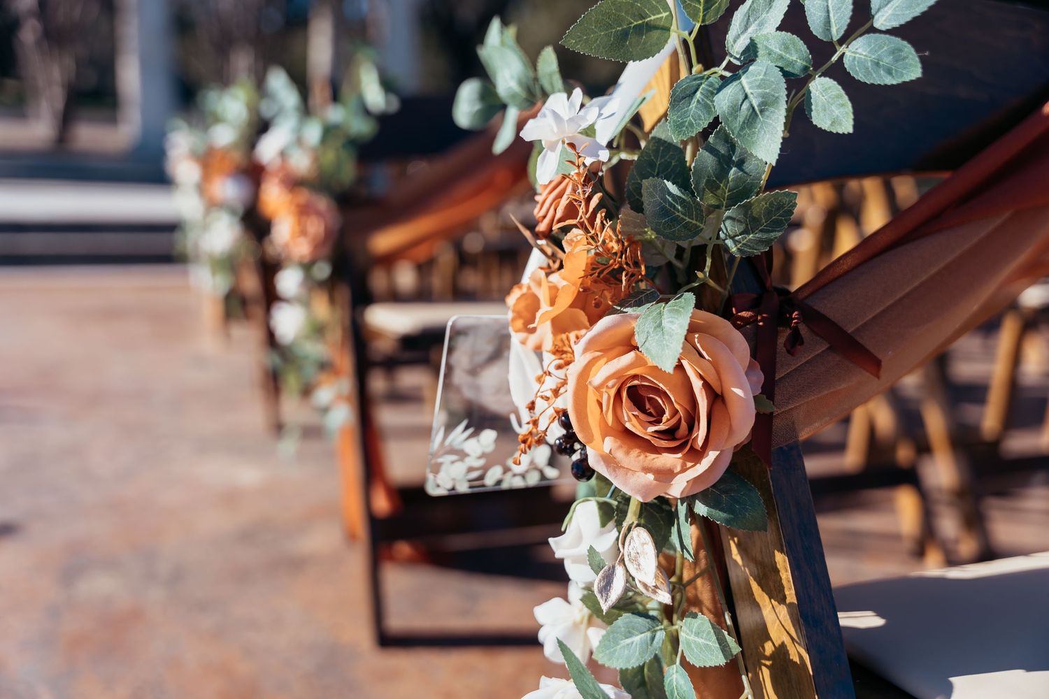 Orange roses and eucalyptus garland decorating wooden ceremony chairs.