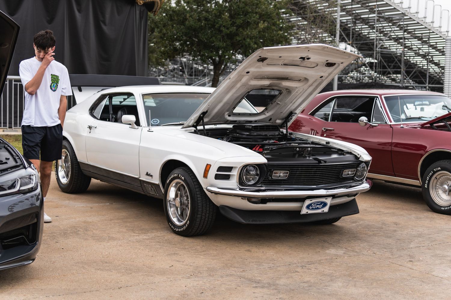 Classic white Ford Mustang with open hood displayed at outdoor car event.
