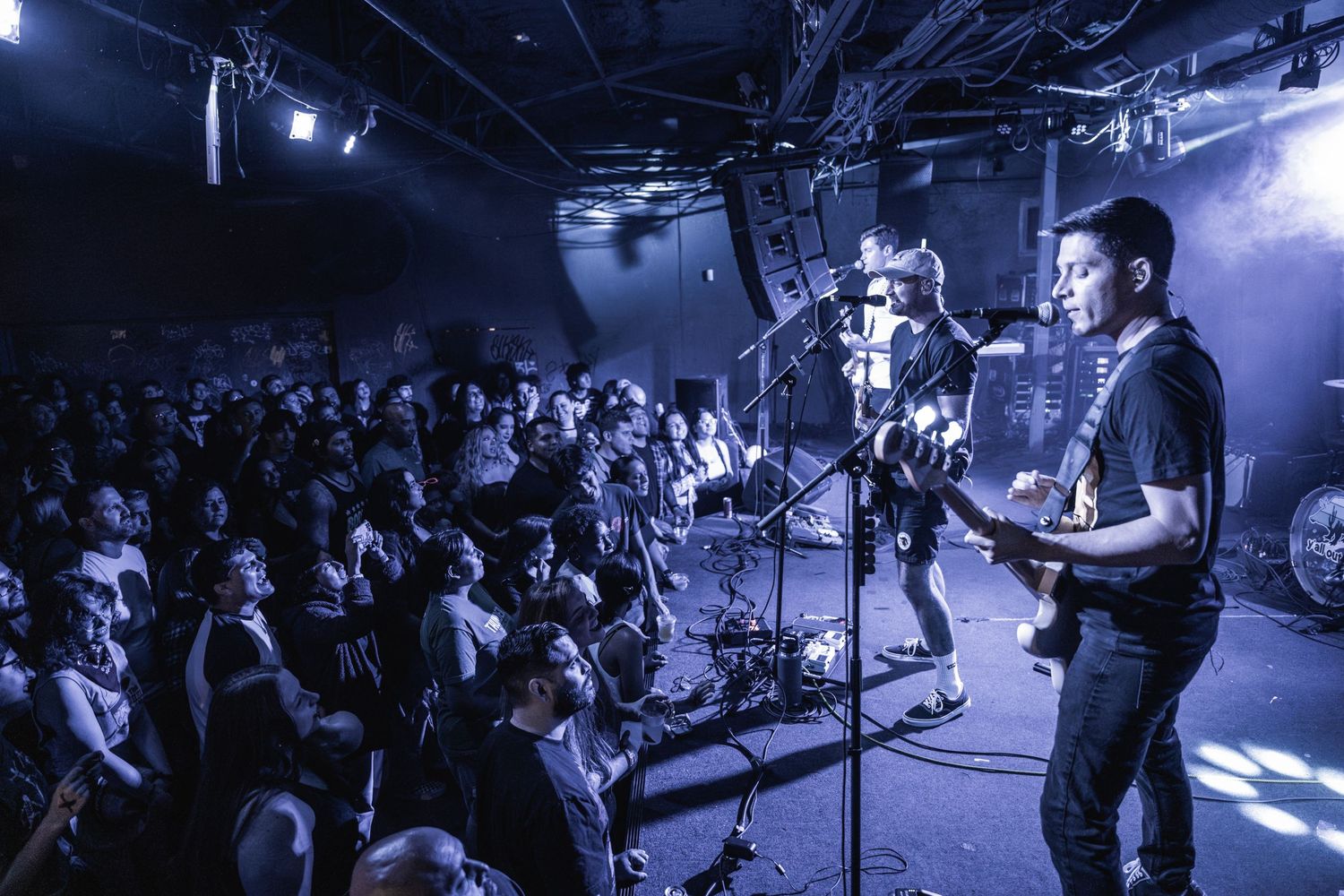 Band performs on stage before packed crowd in small venue with atmospheric blue lighting.