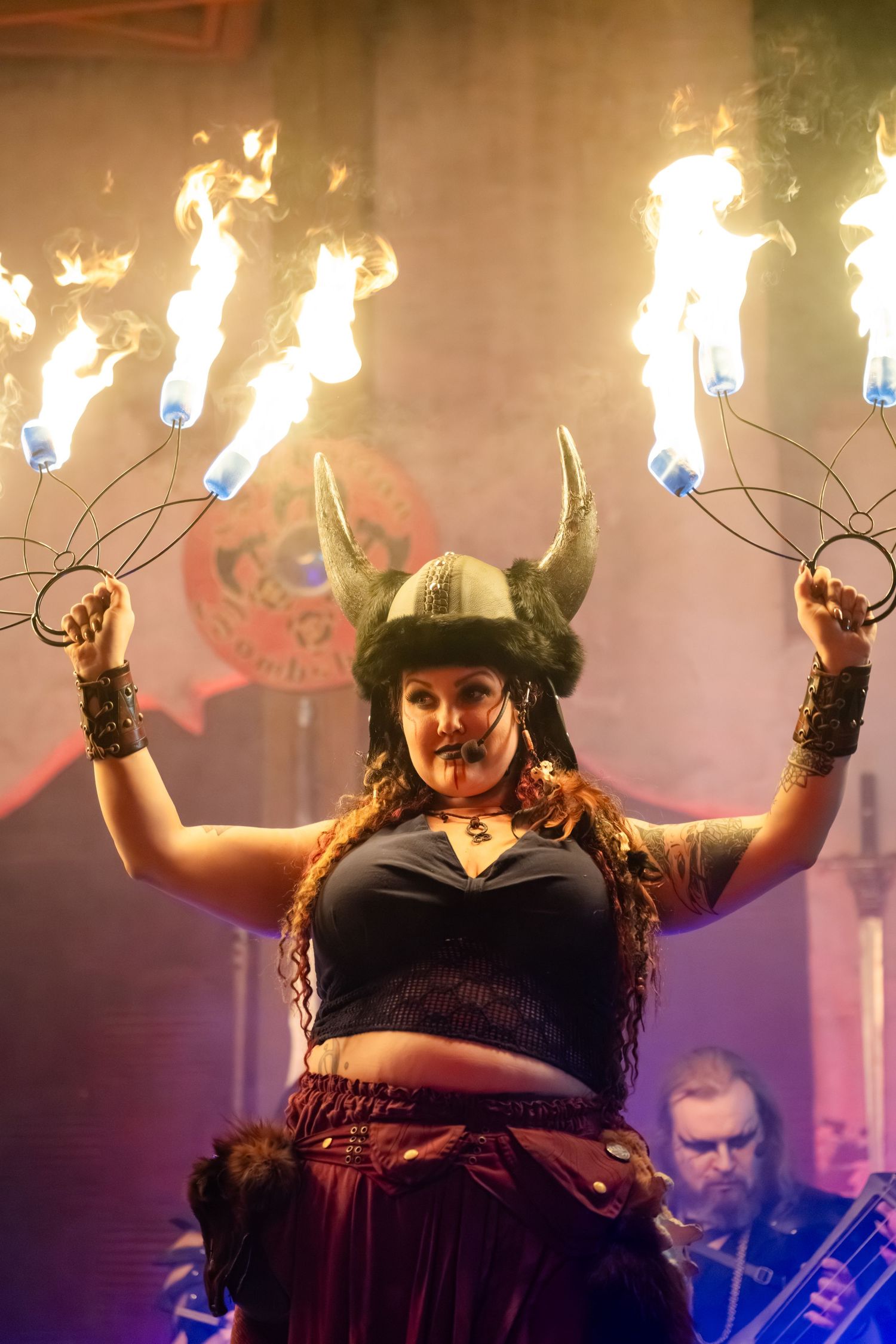A performer in dark clothing holds flaming torches above their head during a dramatic nighttime show.