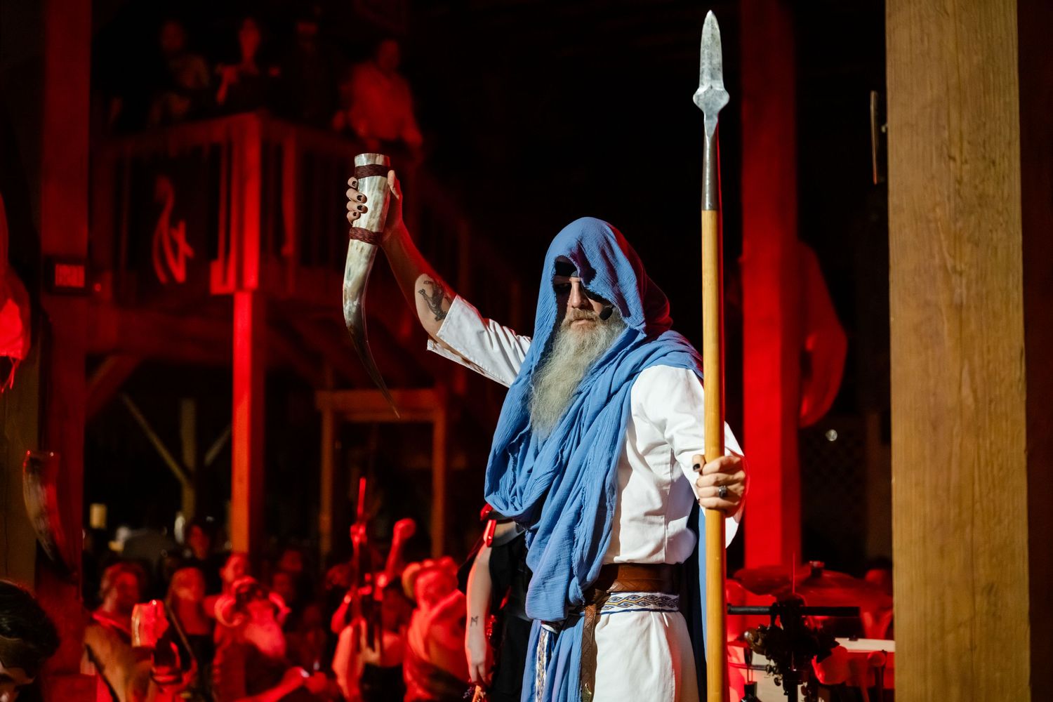 A dramatic performance on stage with red lighting shows performers in blue robes during a theatrical production.