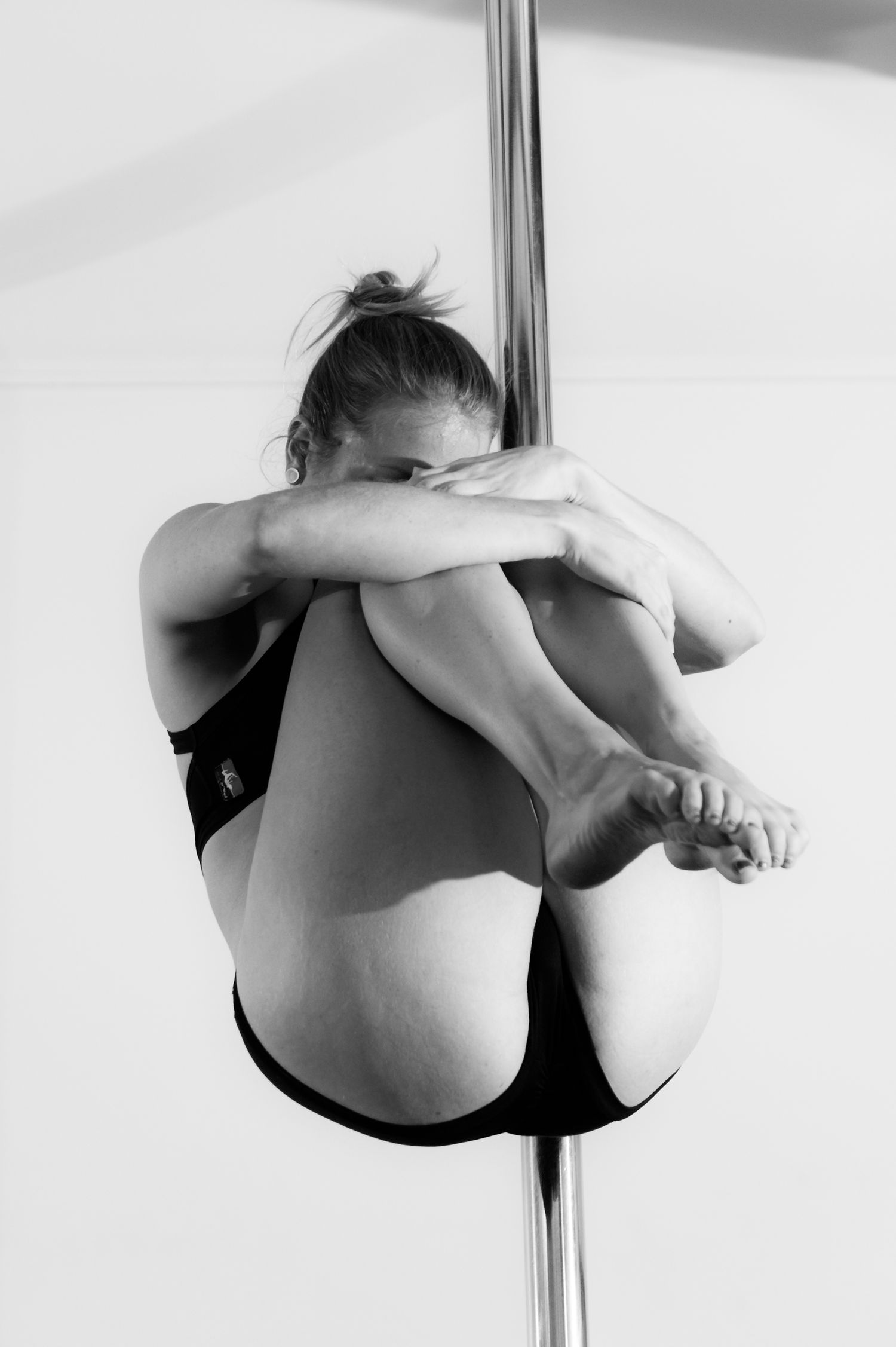 Black and white artistic pole dance performance sequence showing graceful inverted poses against light background.