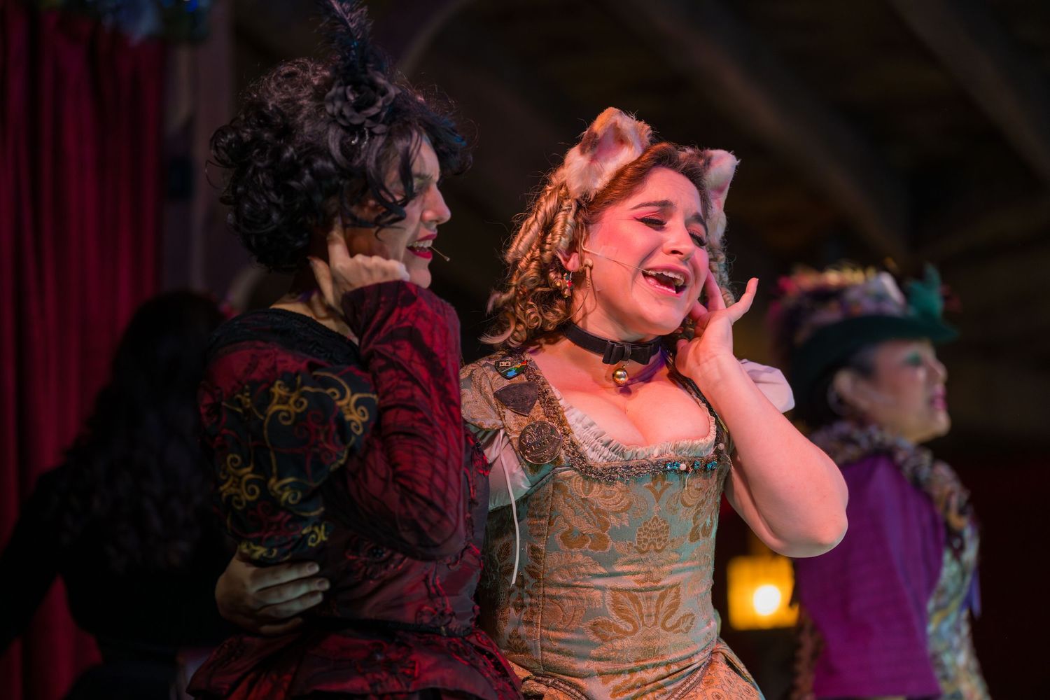Performers in period costumes dance and sing together on a theatrical stage during a dramatic musical production.