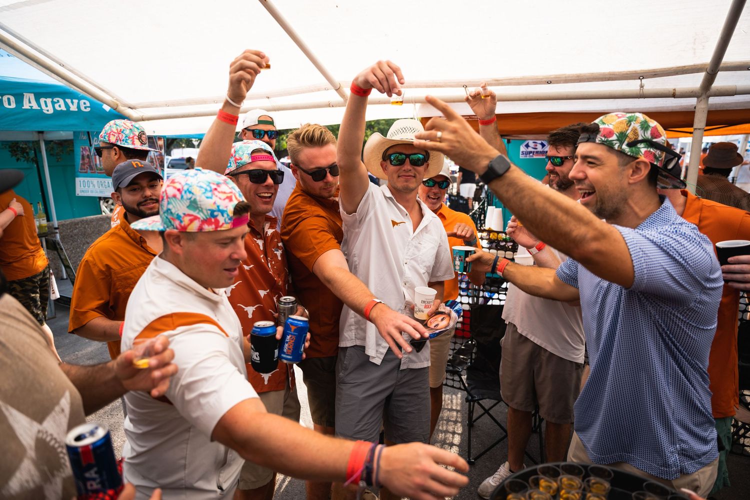A group of sports fans in burnt orange colors celebrate and cheer together at an outdoor tailgate party.