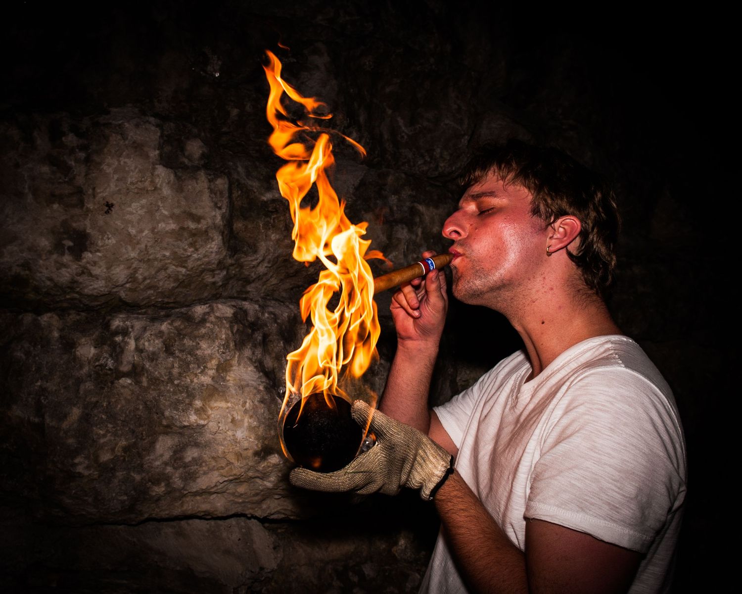 A fire breather performs a sequence of dramatic flame breathing tricks against a dark stone wall background.