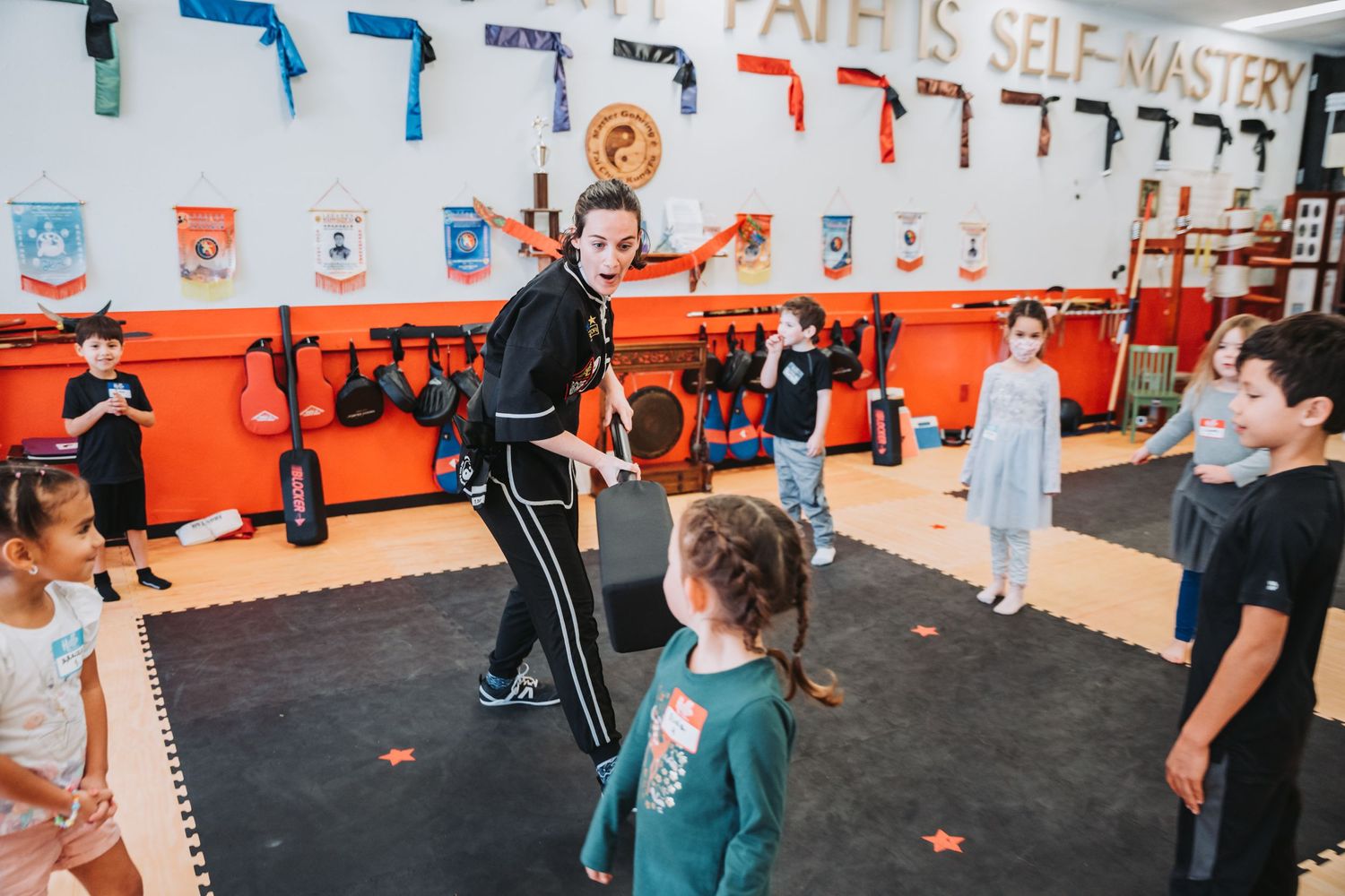Martial arts training class in progress with orange walls and decorative banners.