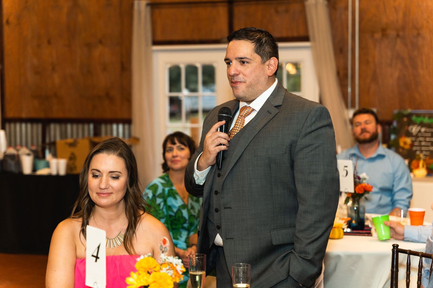Wedding reception toast being given in rustic wooden venue with string lights.