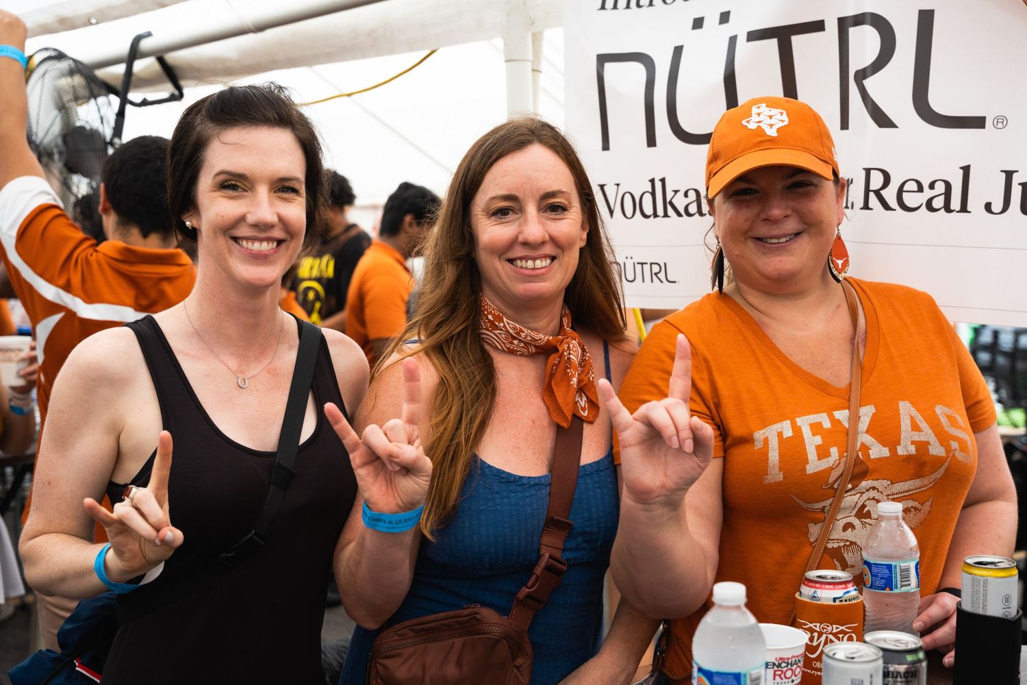 Three people making hook 'em horns gestures at an outdoor Texas event.