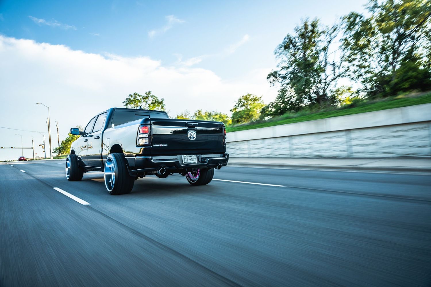 Modified black Chevrolet pickup truck photographed from rear while cruising on road.