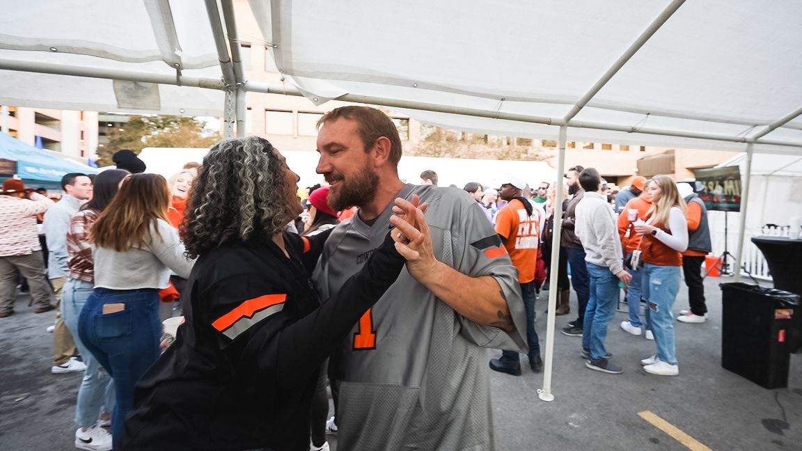 Crowd of people dancing and celebrating under a white tent at an outdoor event.