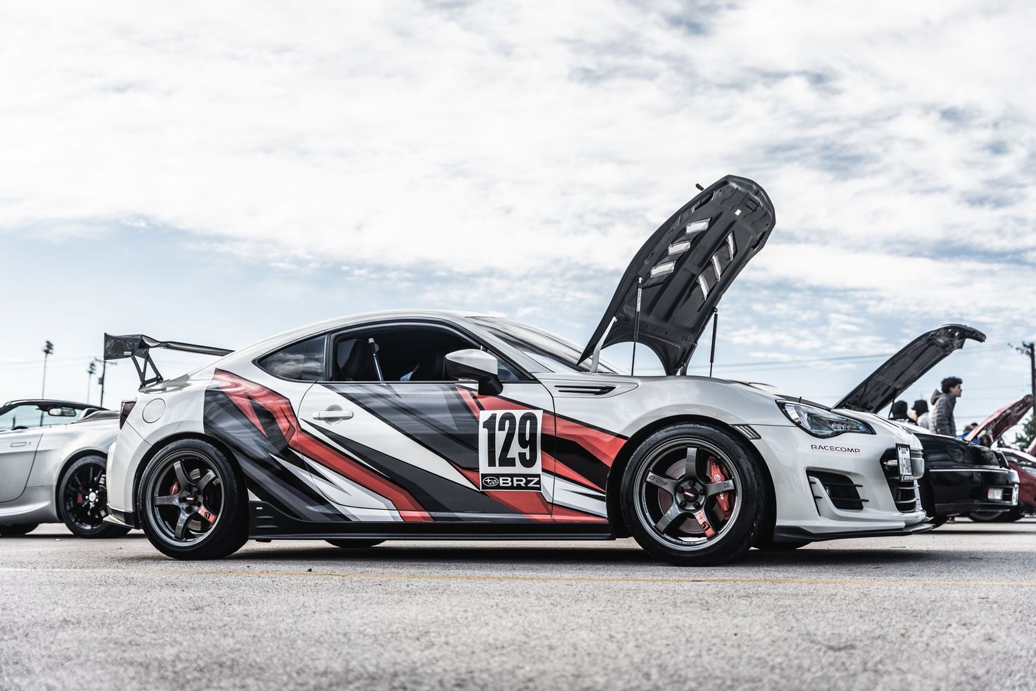 A race-prepped sports car with black and red livery and a raised hood on display.