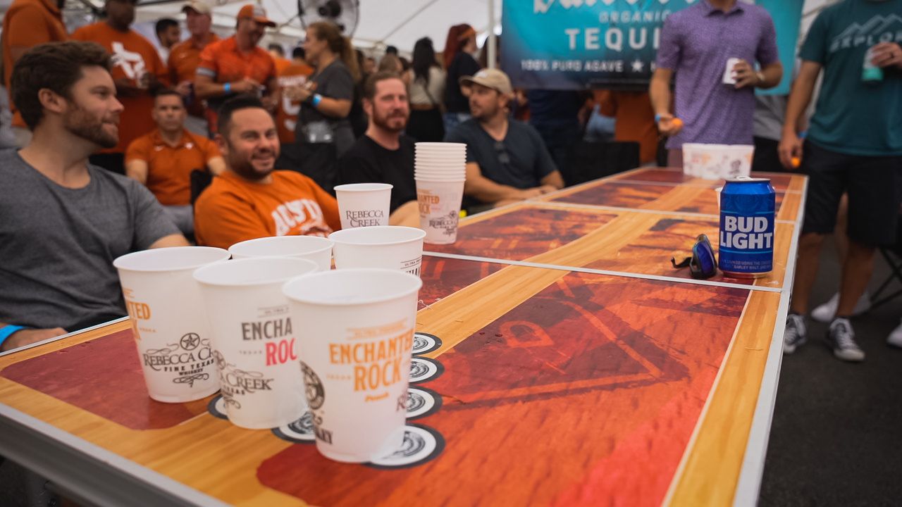 Beer pong setup with plastic cups on decorated table at outdoor gathering.