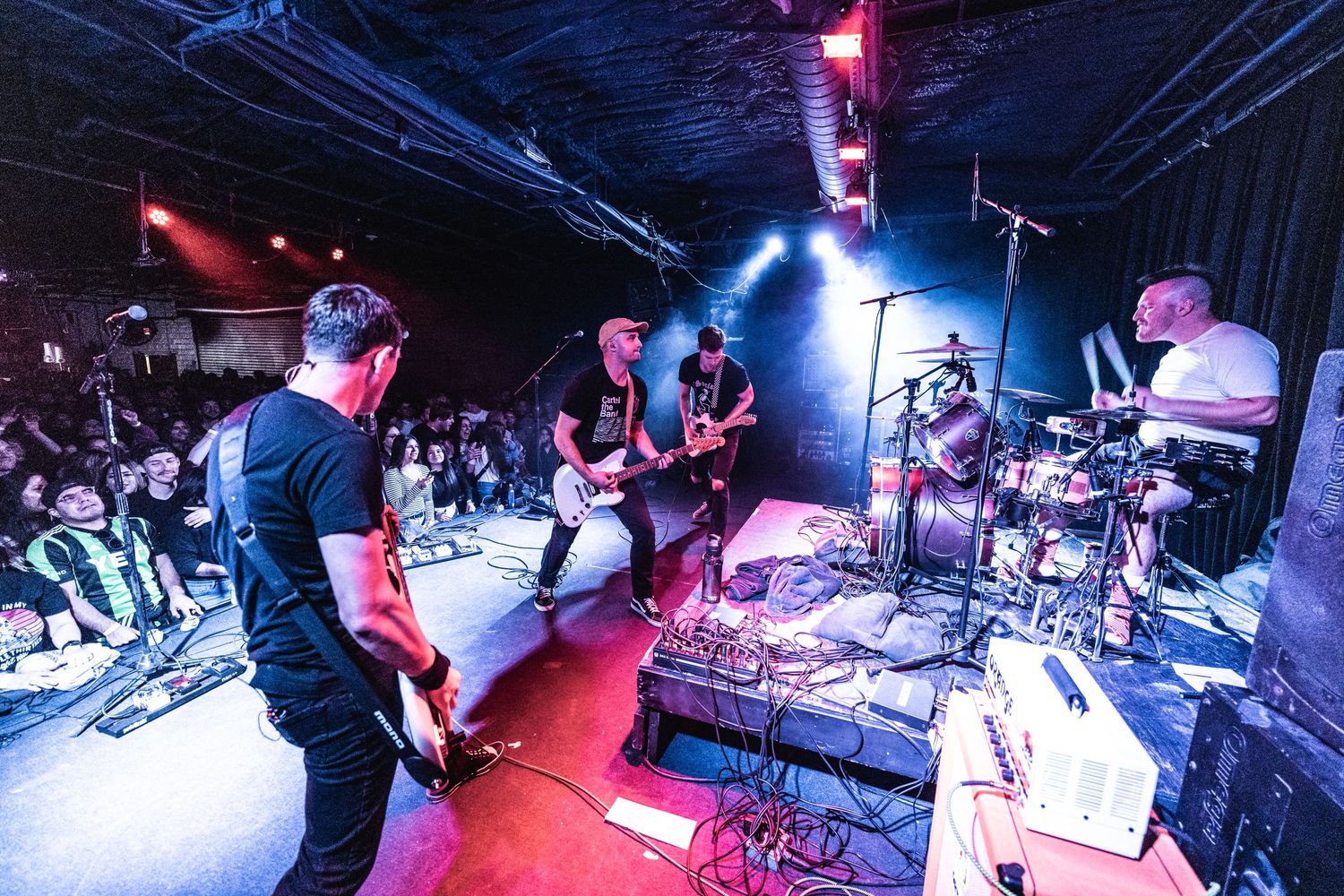 Musicians perform on a red-lit stage with instruments and equipment visible.