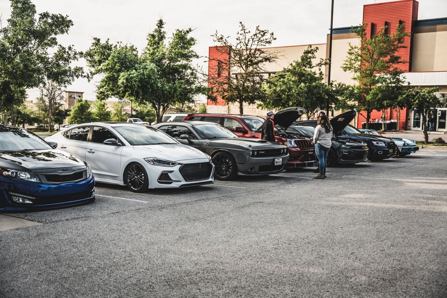 Modern performance cars lined up at an auto show in a retail parking lot.