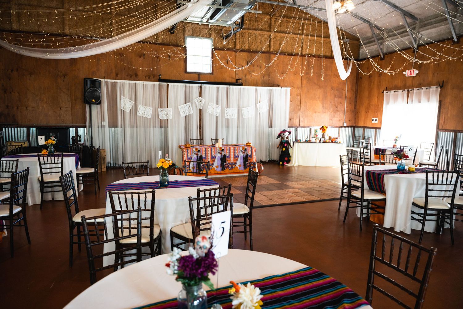 Wedding reception venue with round tables, colorful runners and elegant string light decorations.