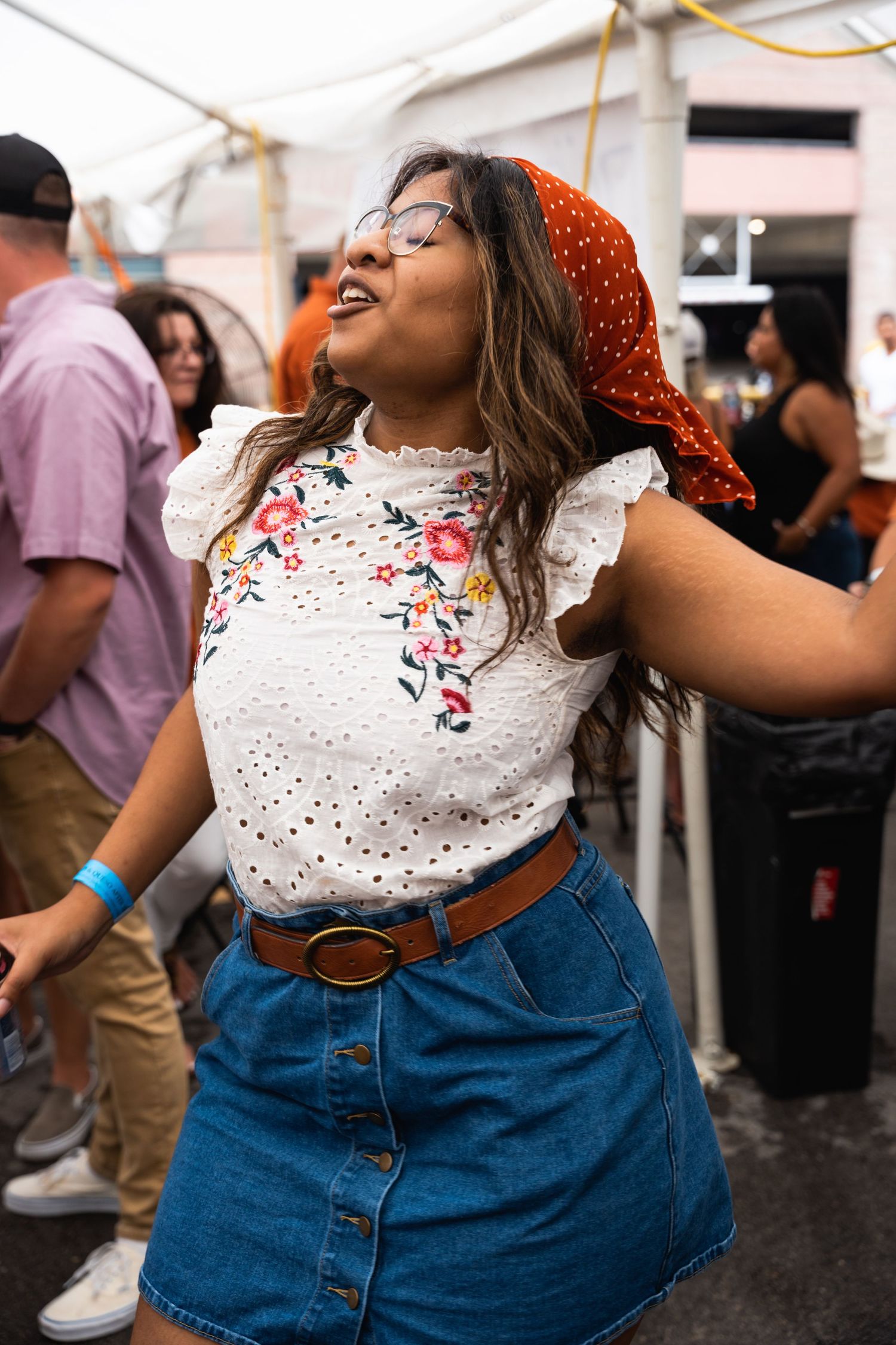 Festival attendee in floral top and denim skirt dancing enthusiastically under tent.