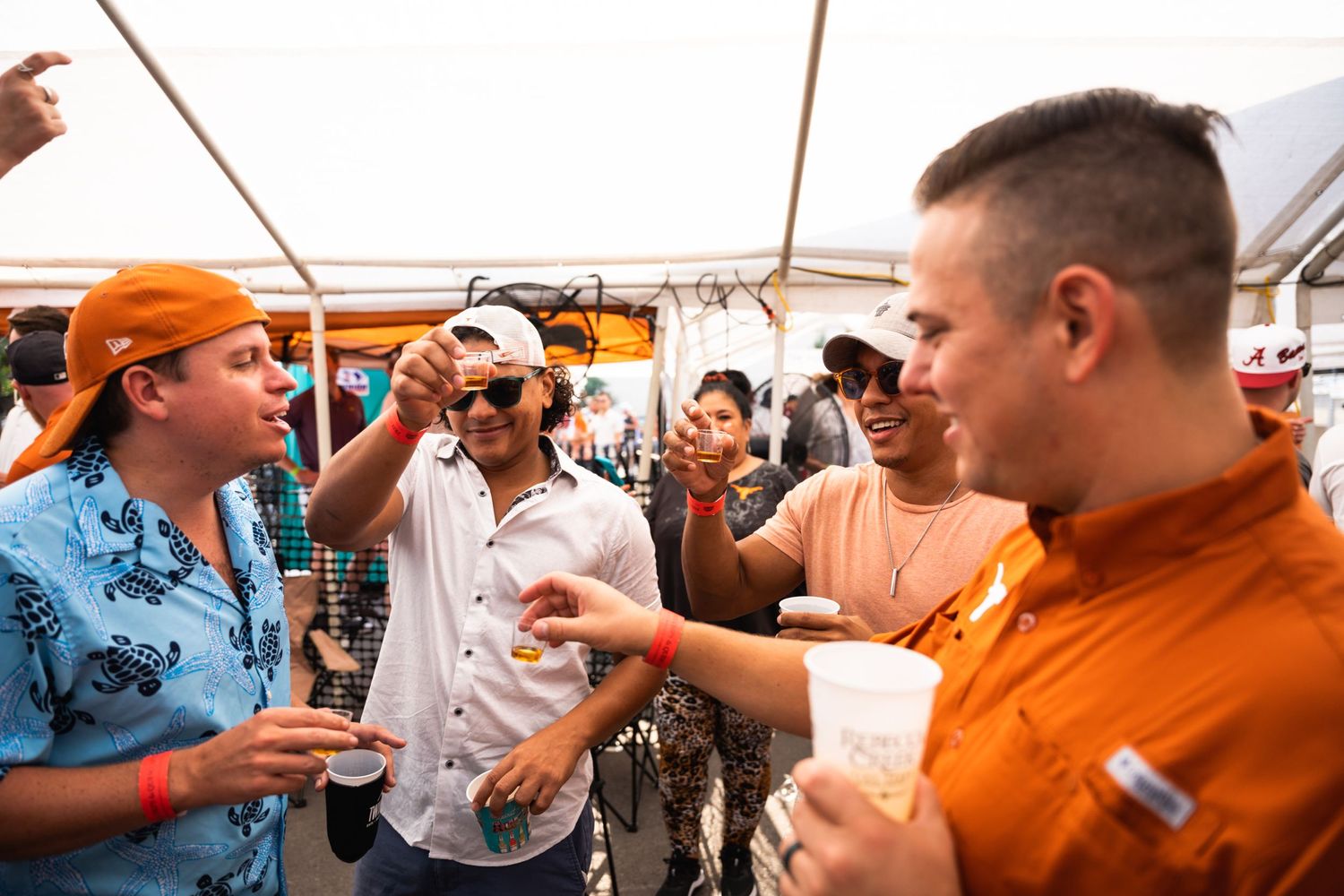 Friends enjoying drinks and conversation under a tent at an outdoor social gathering.