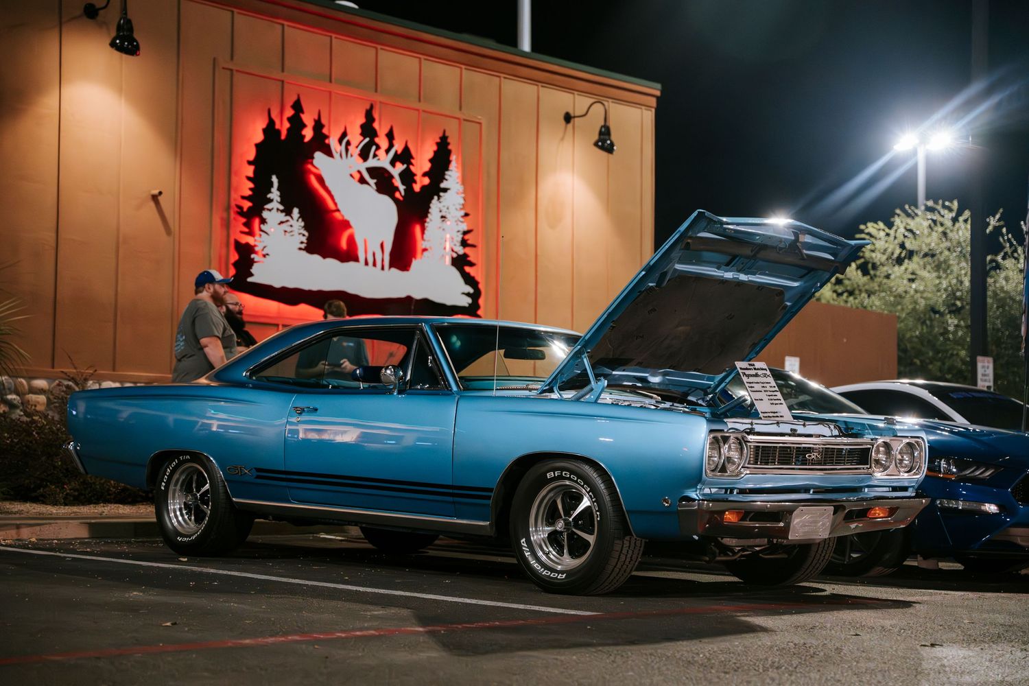 Classic blue muscle car parked at night under illuminated signage.