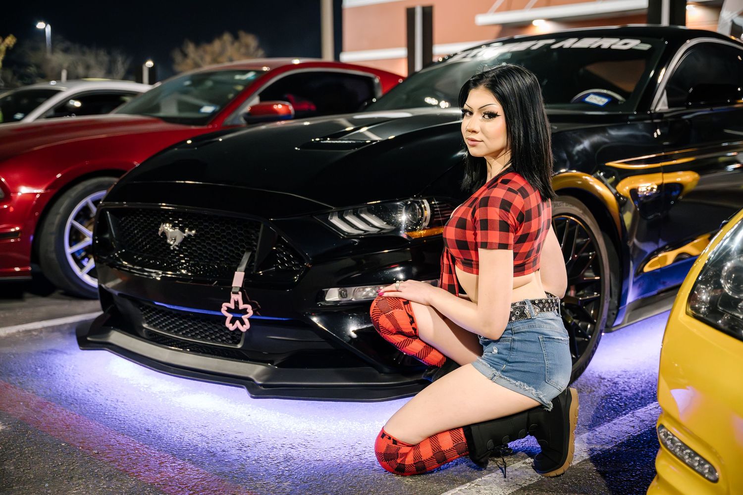 Red and black sports car with custom LED lighting displayed at a nighttime car show.