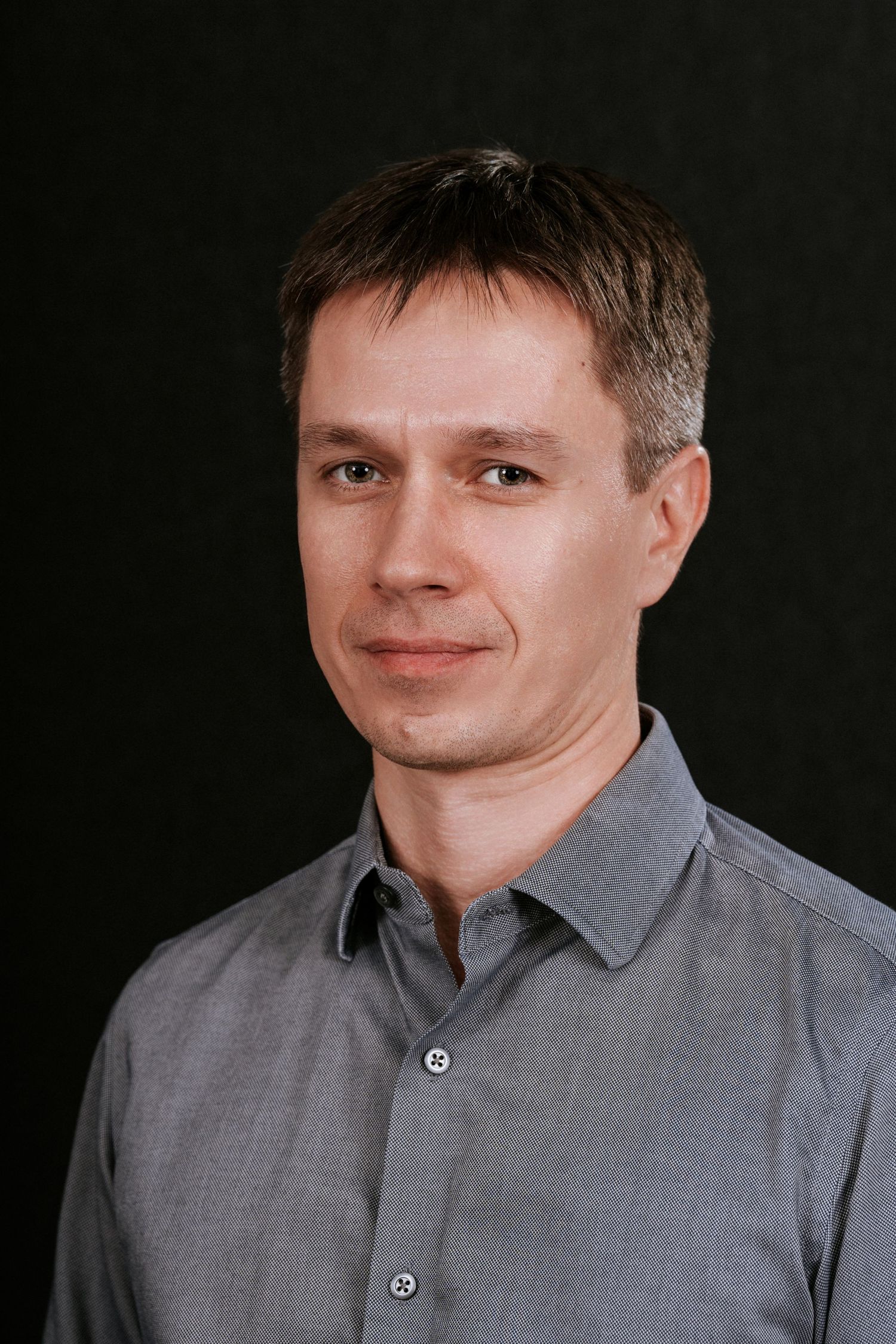 Portrait of person in grey button-down shirt against black backdrop.