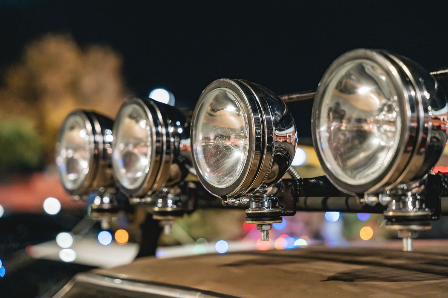 Row of off-road spotlights mounted on vehicle with bokeh background at night.