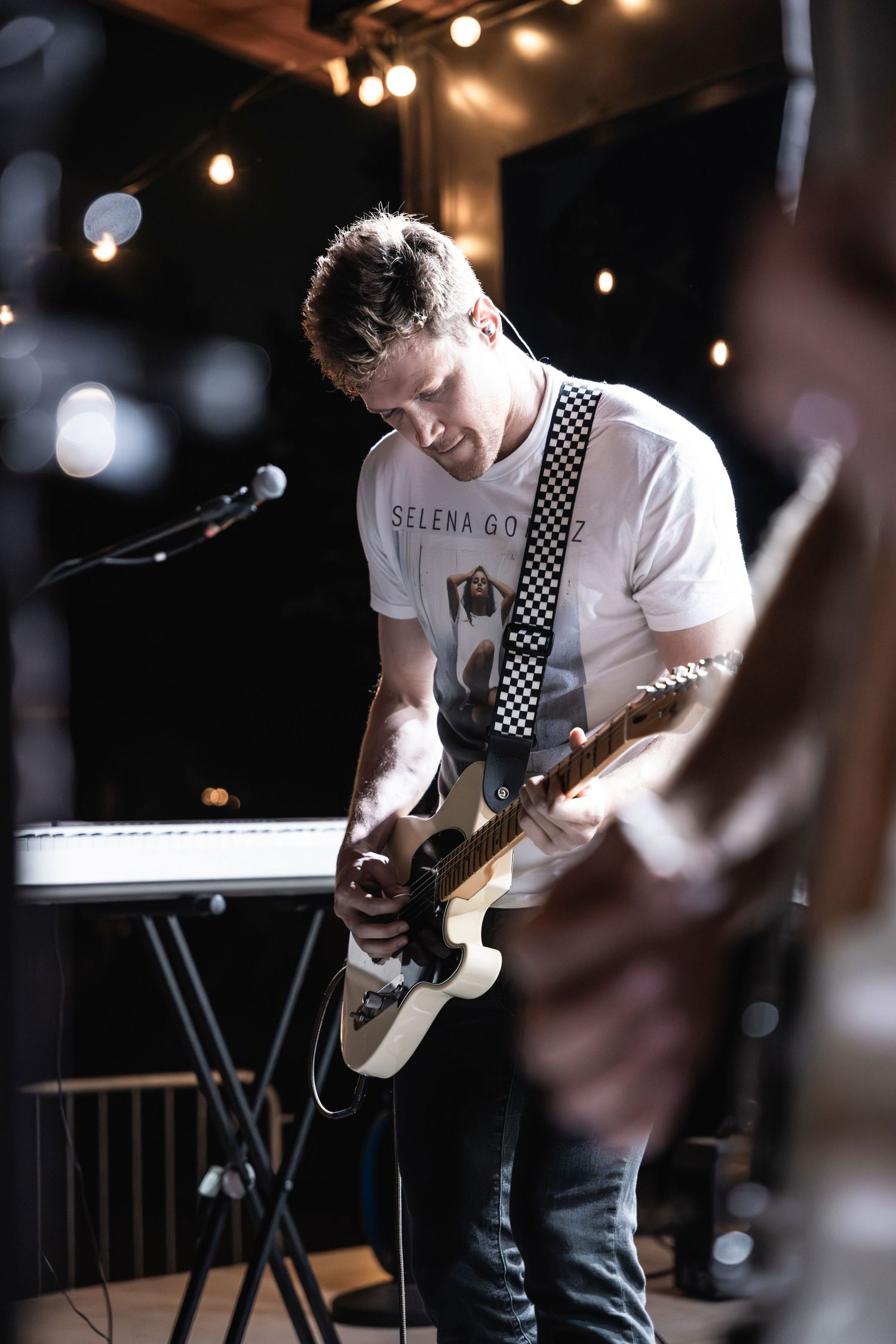 Musician playing electric guitar under string lights during a live performance.