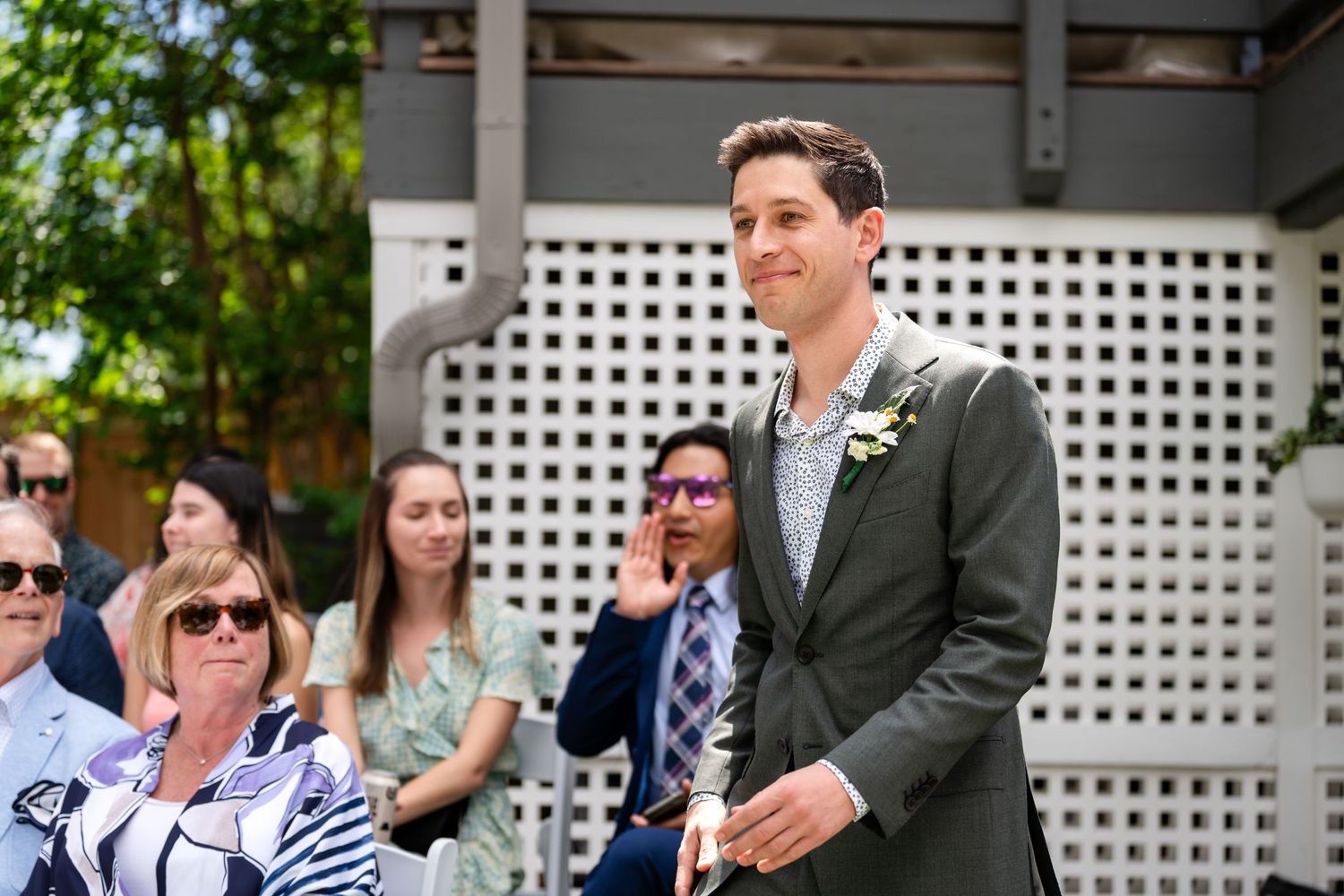 Person in formal attire with boutonniere speaking at outdoor event.