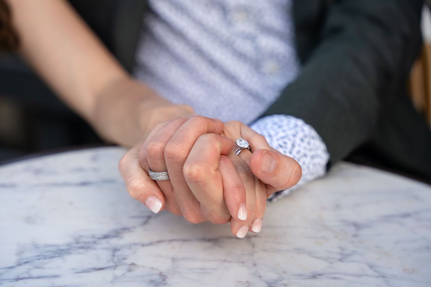 Close-up of newlyweds holding hands showing wedding rings on marble table.