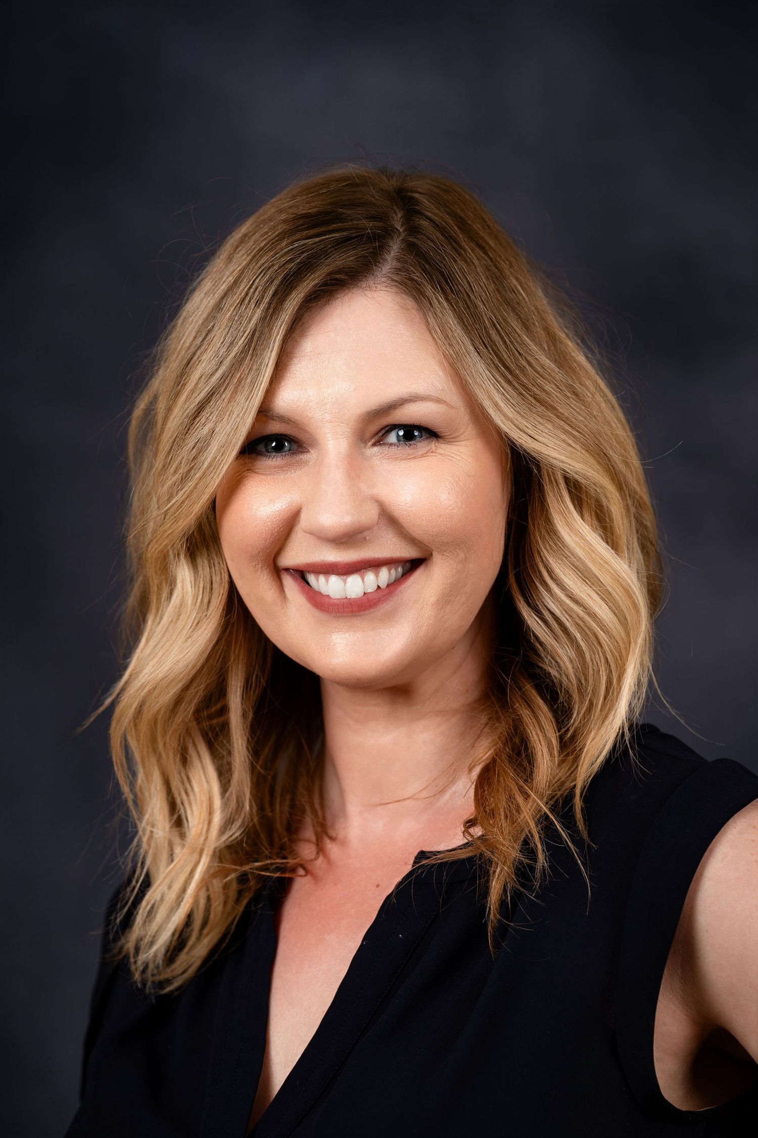 Professional portrait with medium wavy blonde hair and black sleeveless top.