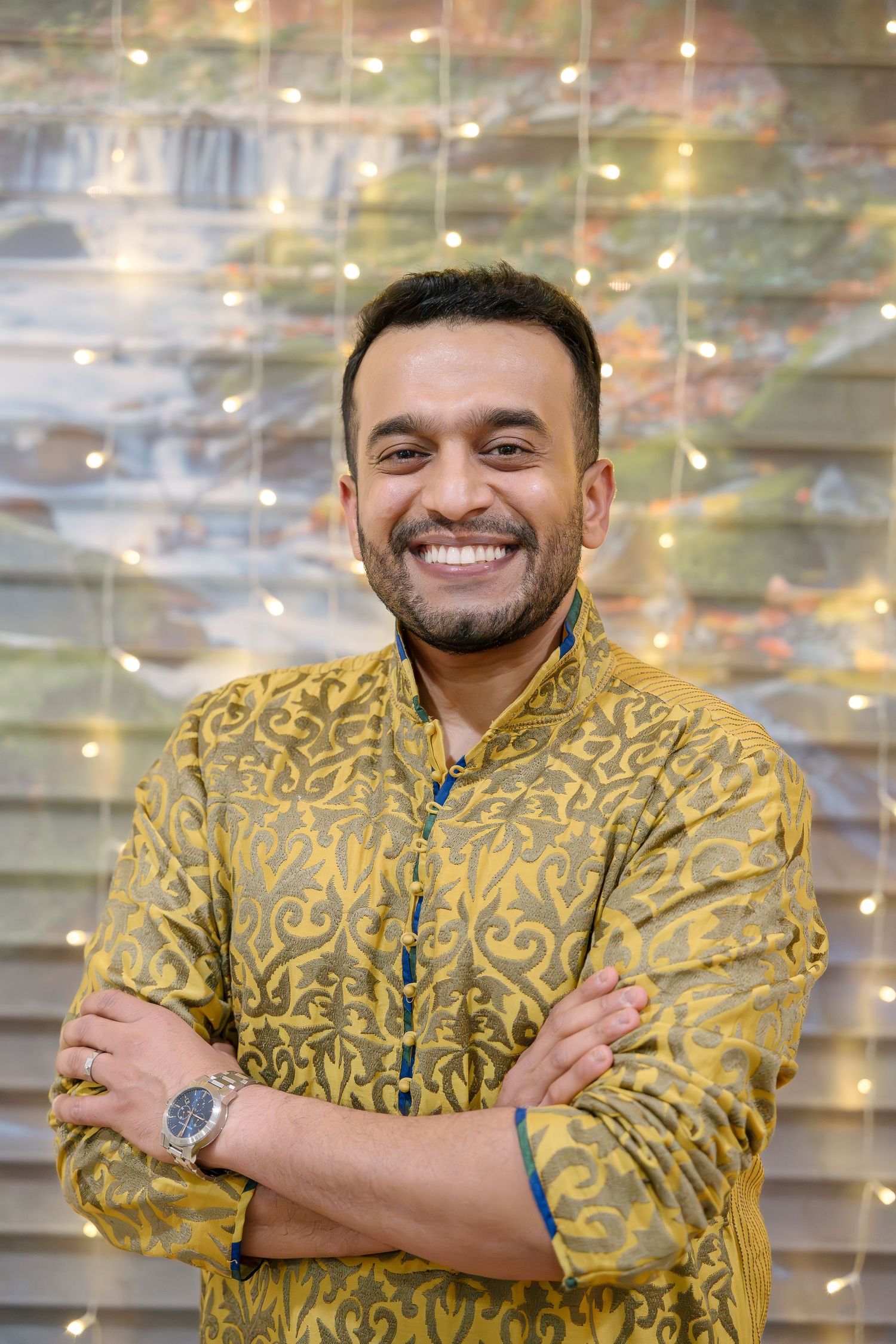 Person wearing a golden embroidered traditional kurta smiles warmly against a sparkly background.