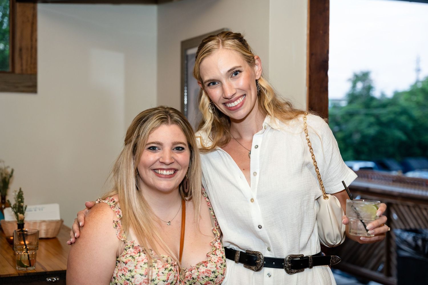 Two women smiling together at a casual indoor gathering.