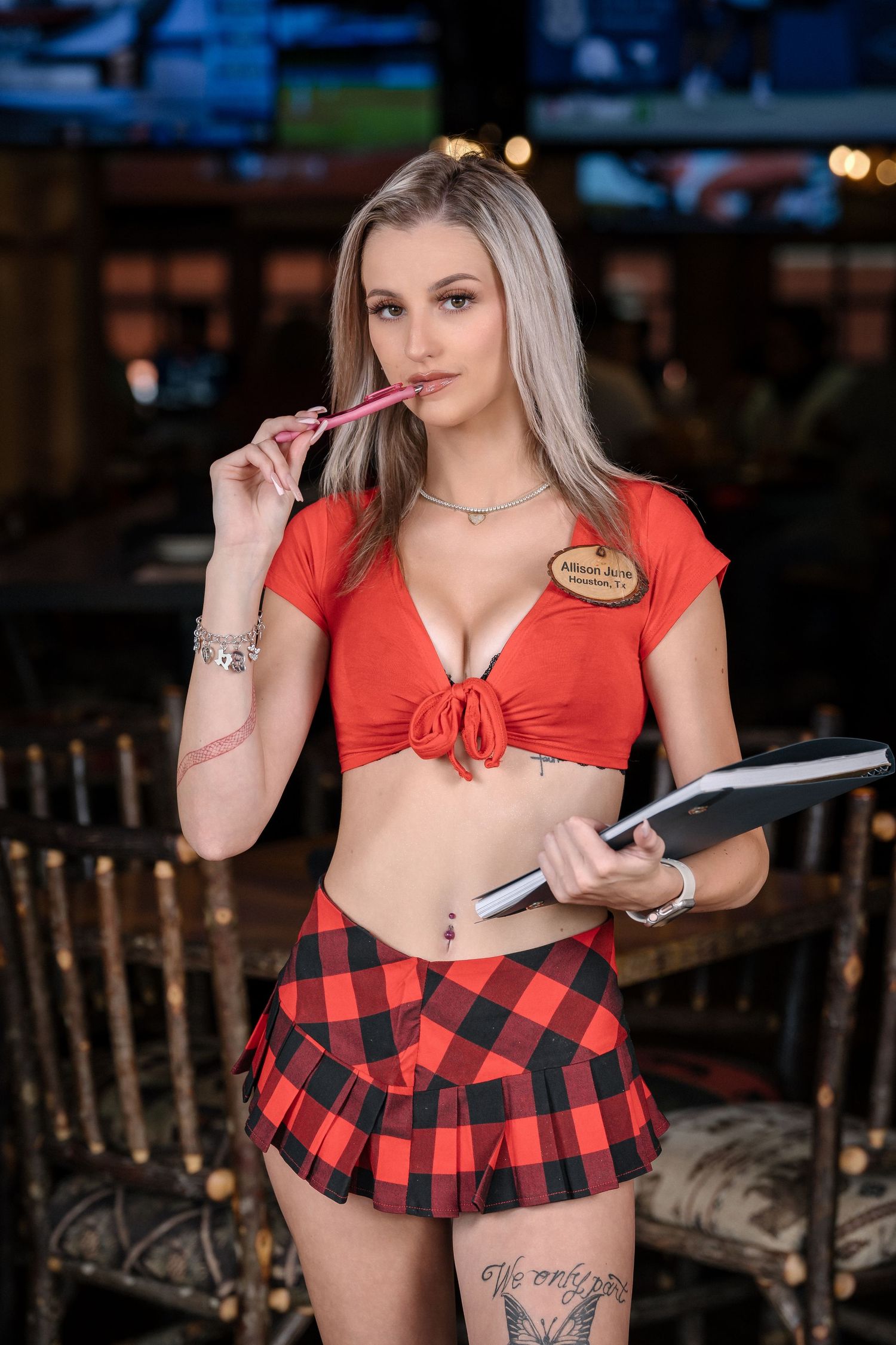 Restaurant server in red tied top and plaid skirt holds pen and notepad.