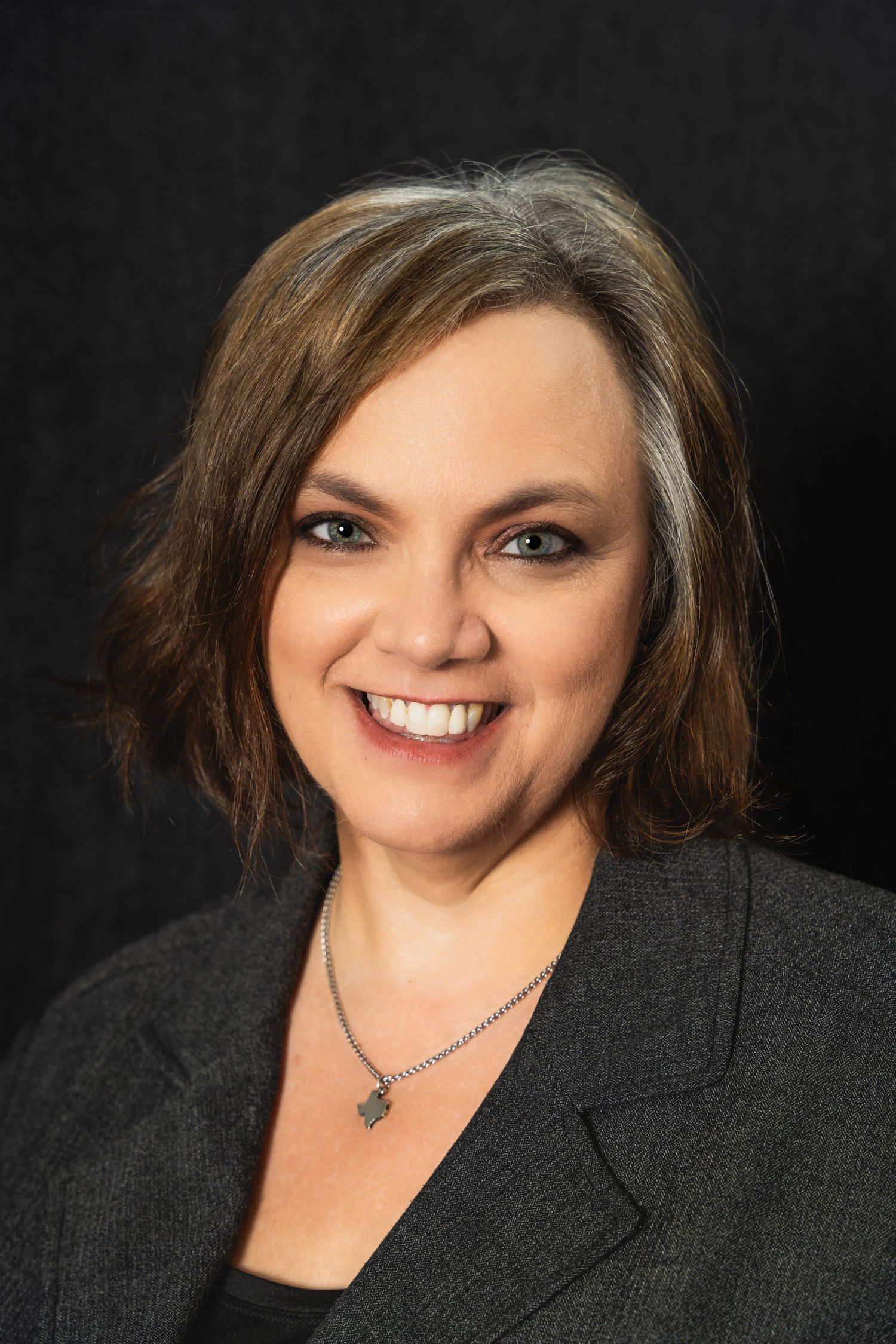 Professional headshot featuring dark blazer and silver necklace with warm expression.