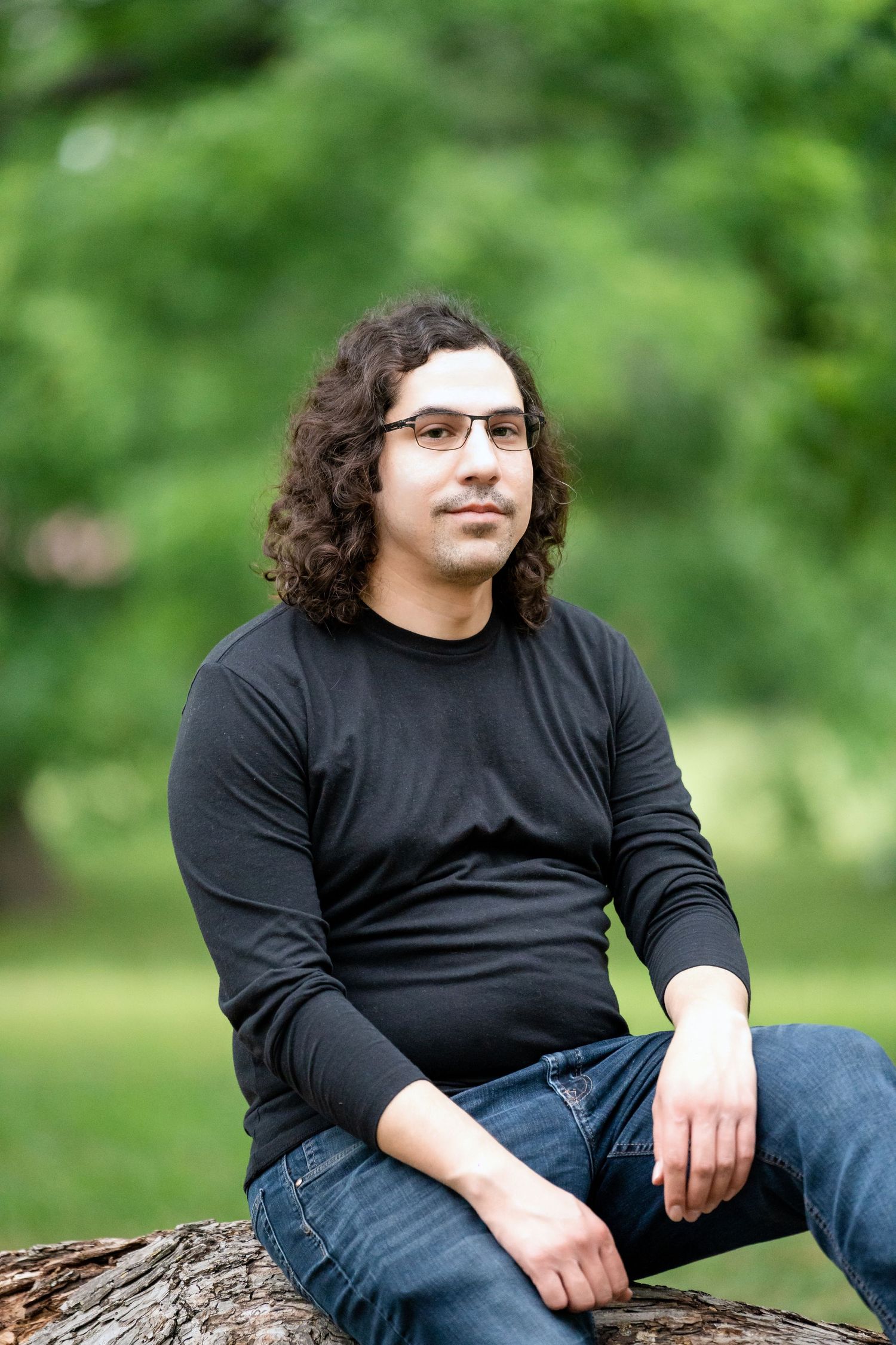 Casual outdoor portrait seated on a log with natural green background.