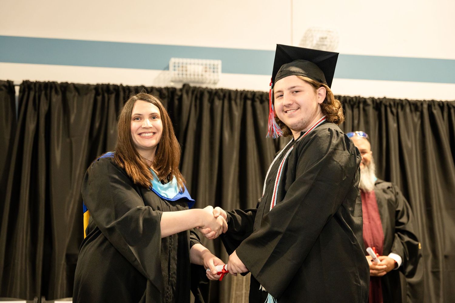 Graduate and faculty member shake hands during diploma presentation at graduation ceremony.