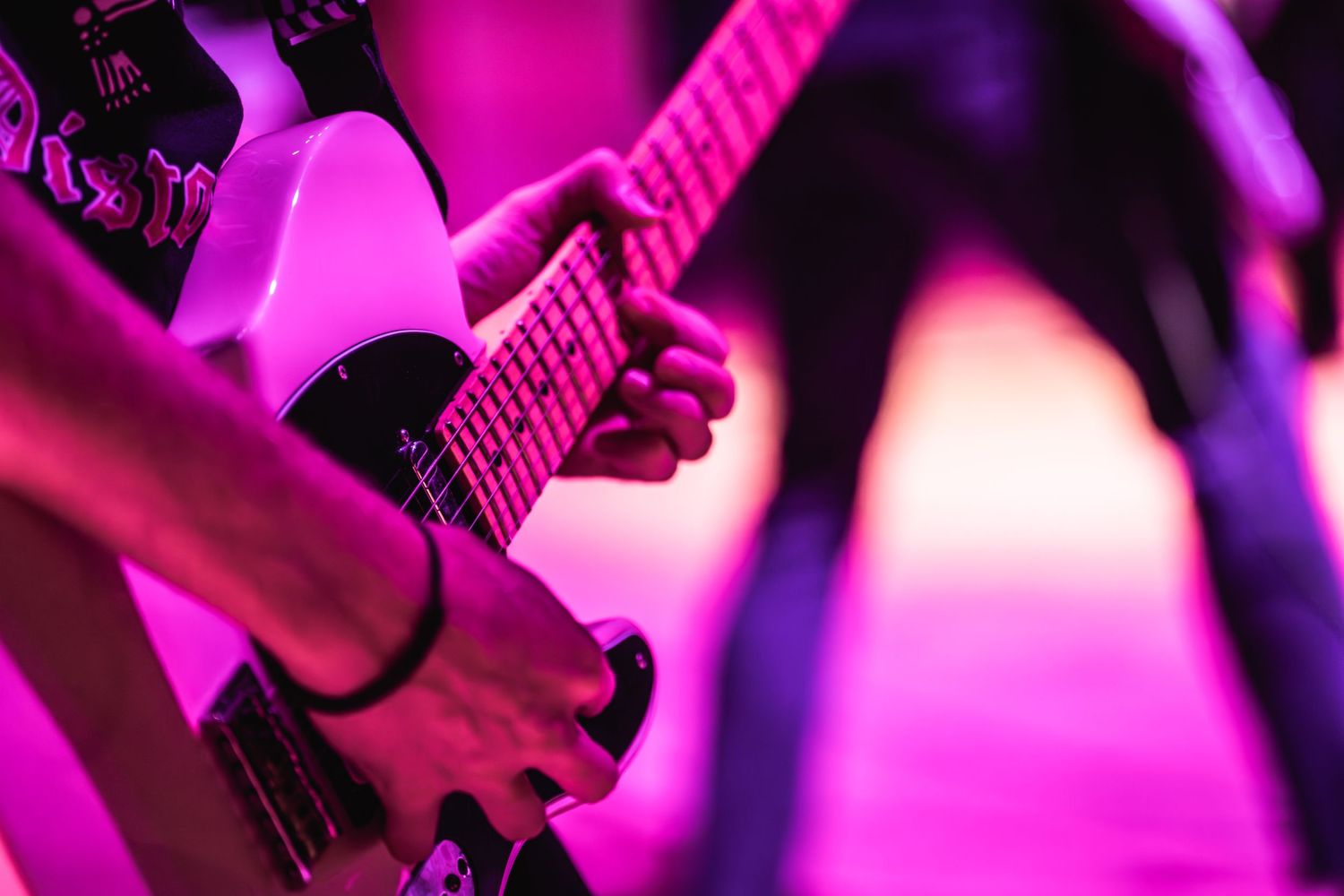 Close-up of guitar being played under vibrant purple stage lighting.
