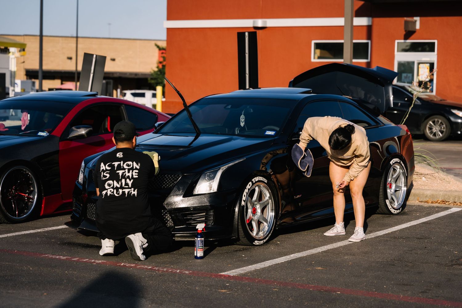 Car enthusiasts examining a black sports car at an outdoor car meet.