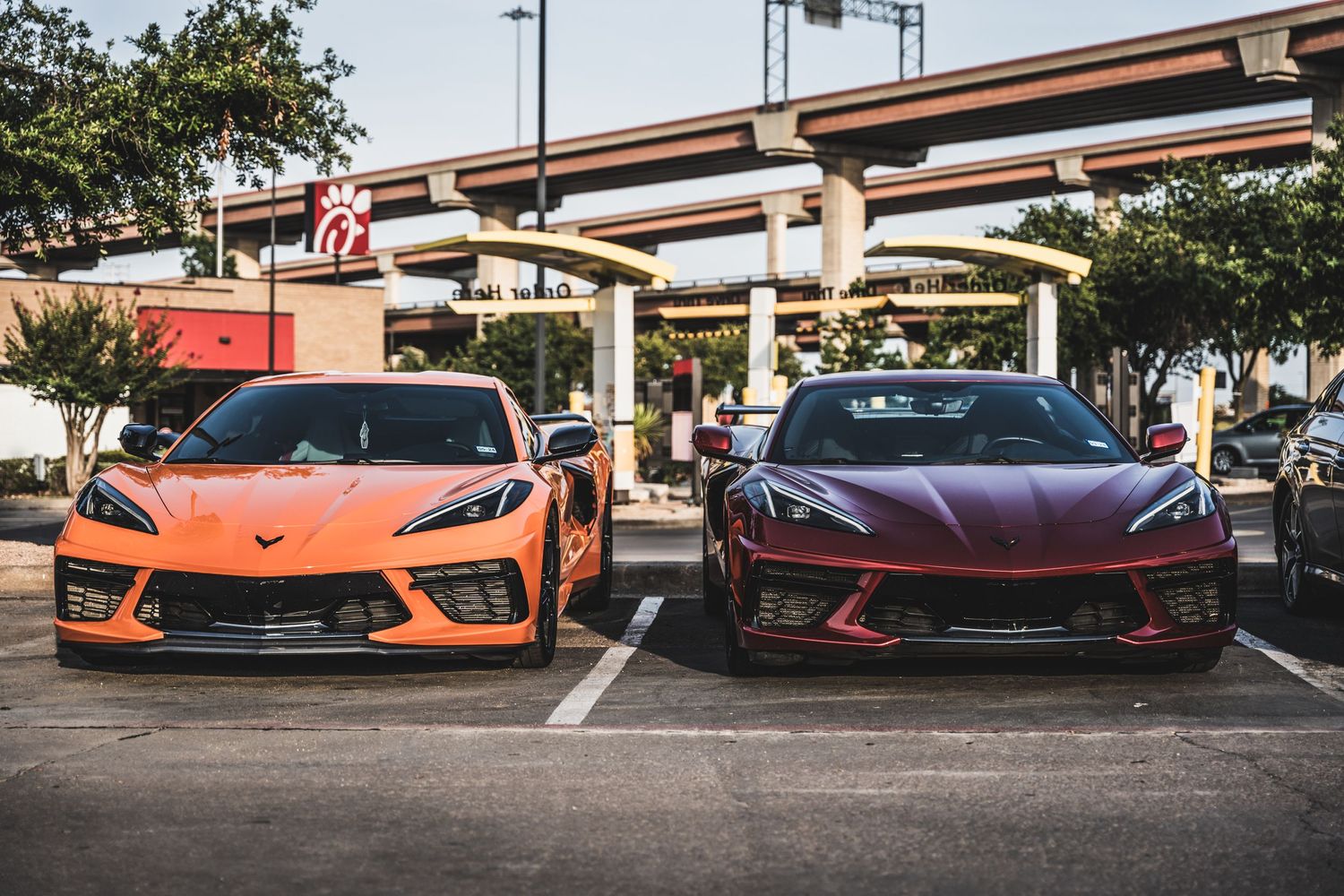 Orange and burgundy Chevrolet Corvettes parked side by side in a parking lot.