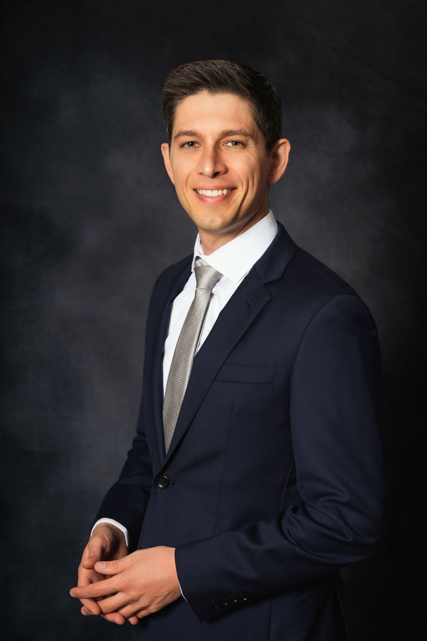 Business portrait of person in dark suit smiling against studio background.