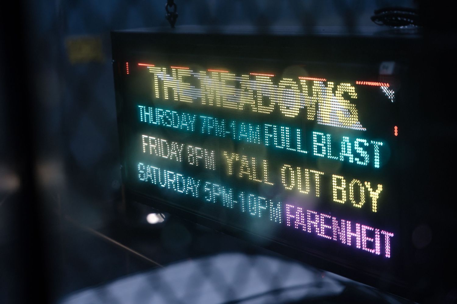 Neon sign displaying performance schedule with Fall Out Boy and other band names in blue lighting.