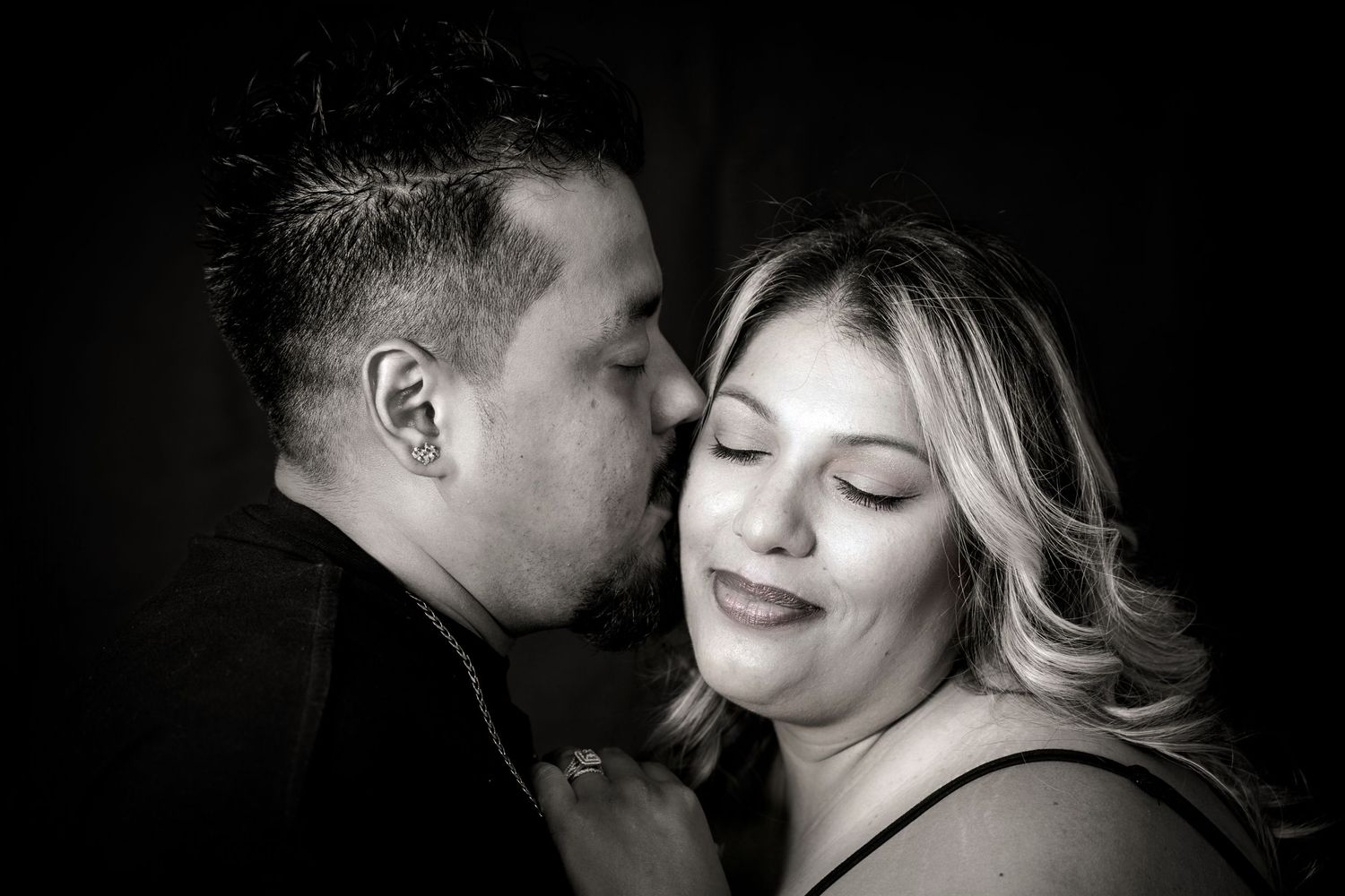 Romantic black and white portrait of couple sharing an intimate moment against dark backdrop.