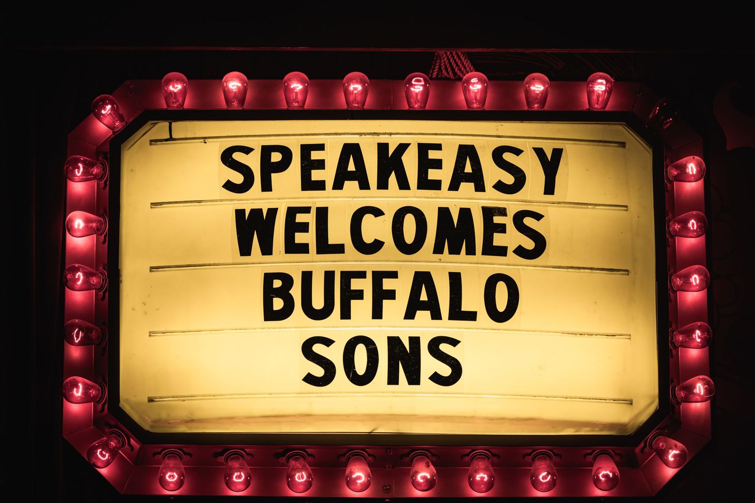Vintage-style marquee sign with red lights reading 'Speakeasy Welcomes Buffalo Sons'.