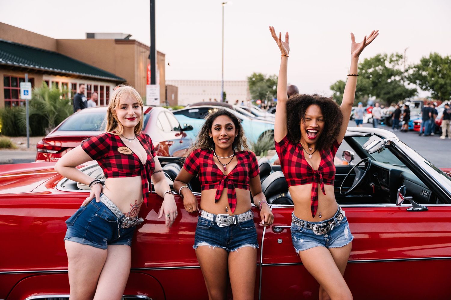 Friends celebrating and posing by classic red car at outdoor event.