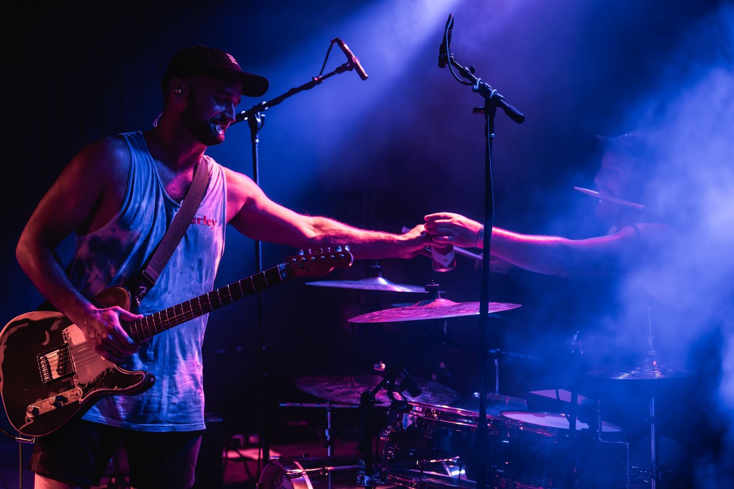 Musician plays guitar while singing into microphone with blue lighting effects on stage.