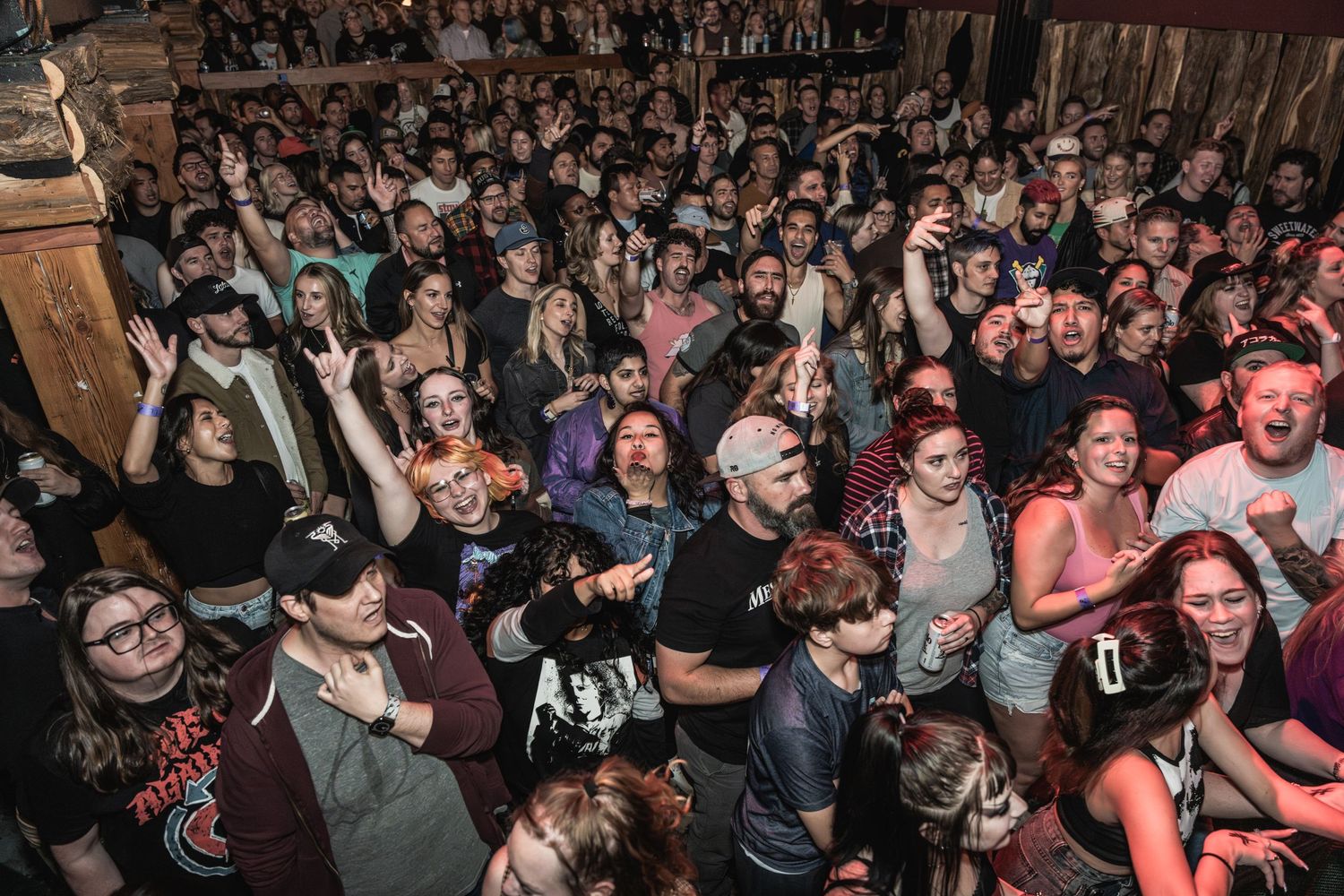 Large enthusiastic crowd fills venue floor during live music performance.